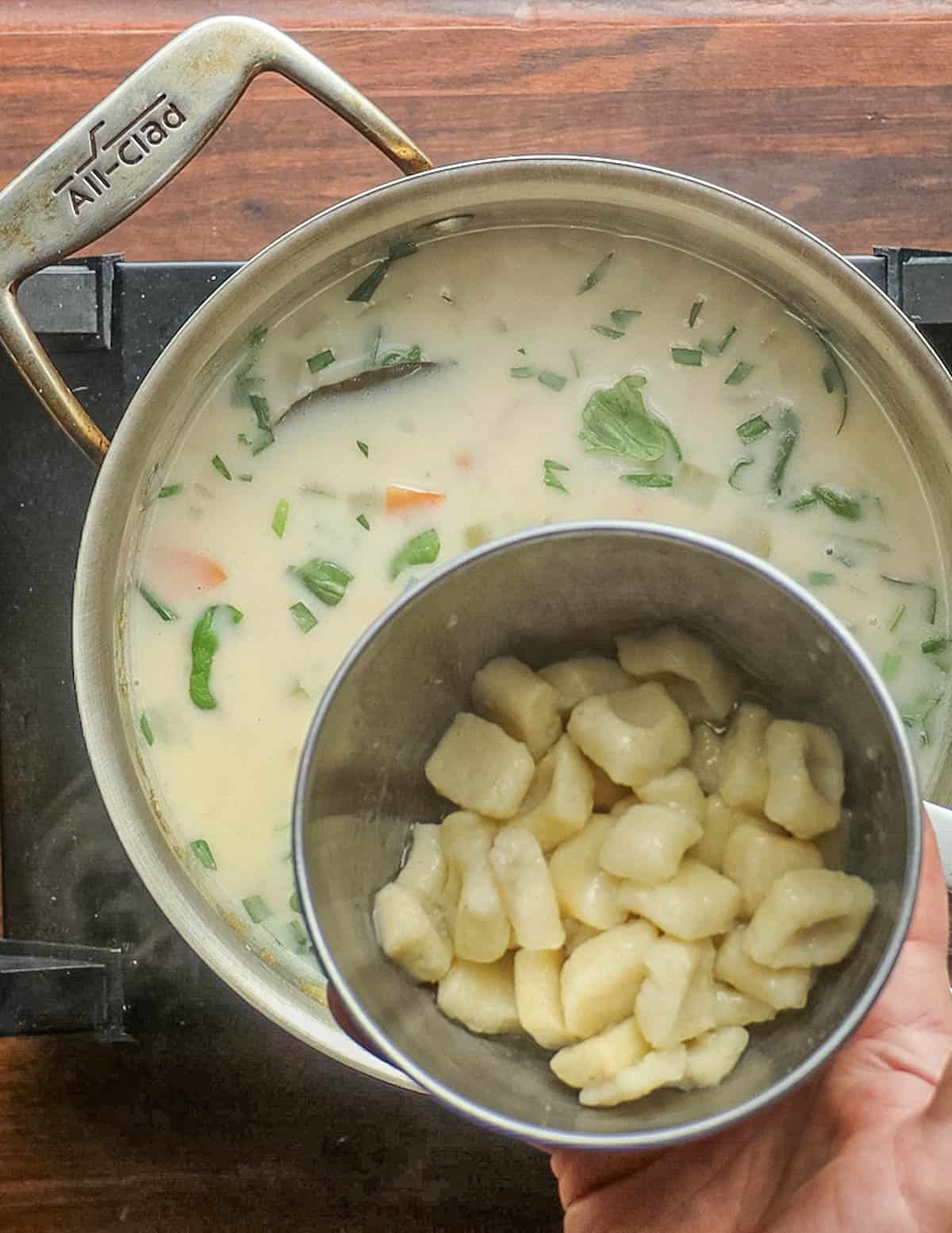 Adding cooked gnocchi dumplings to a pot of soup. 