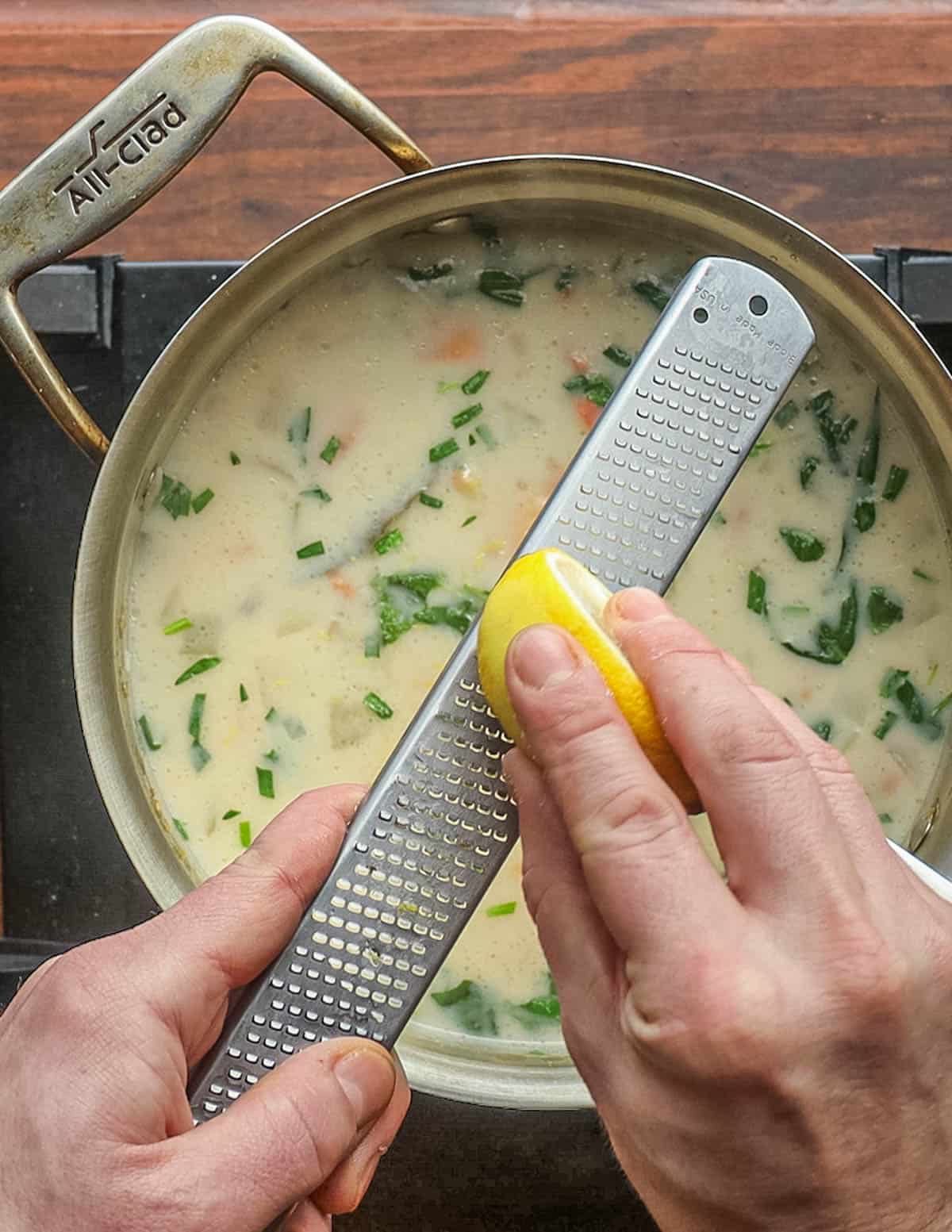 Grating lemon zest into a pot of soup. 