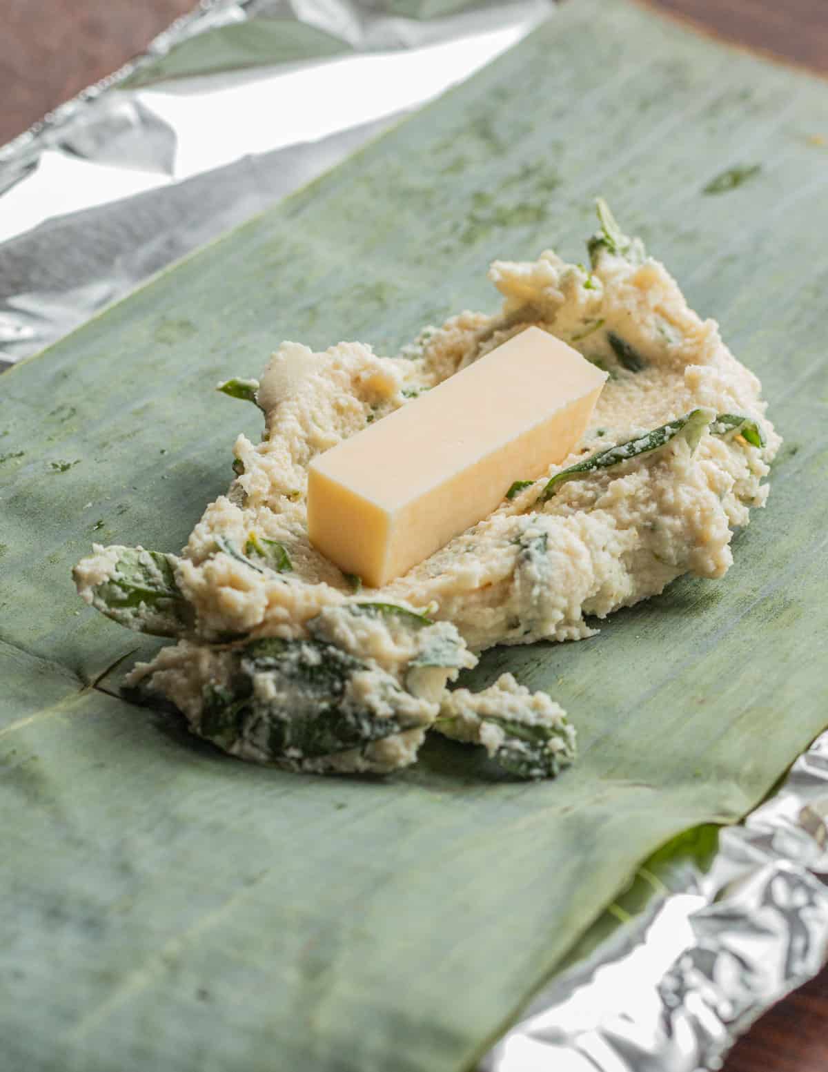 Adding a piece of cheese to a spoonful of masa on a banana leaf. 