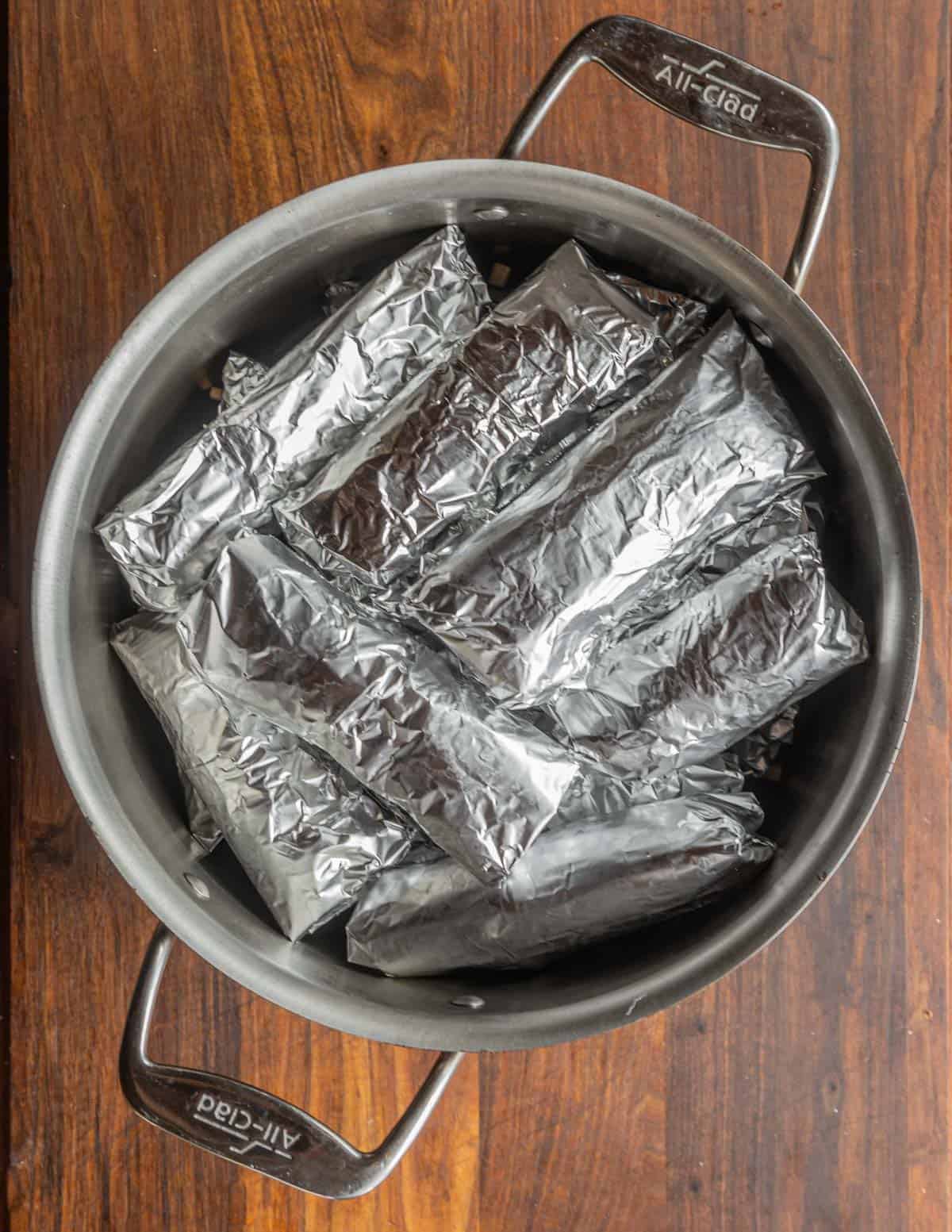 Many chipilin tamales steaming in a pot wrapped in aluminum foil. 