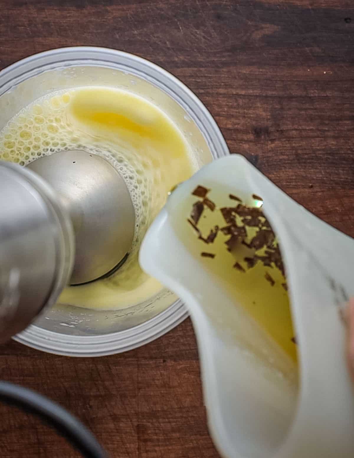 Slowly pouring truffle infused olive oil into container of egg being pureed with a hand blender. 