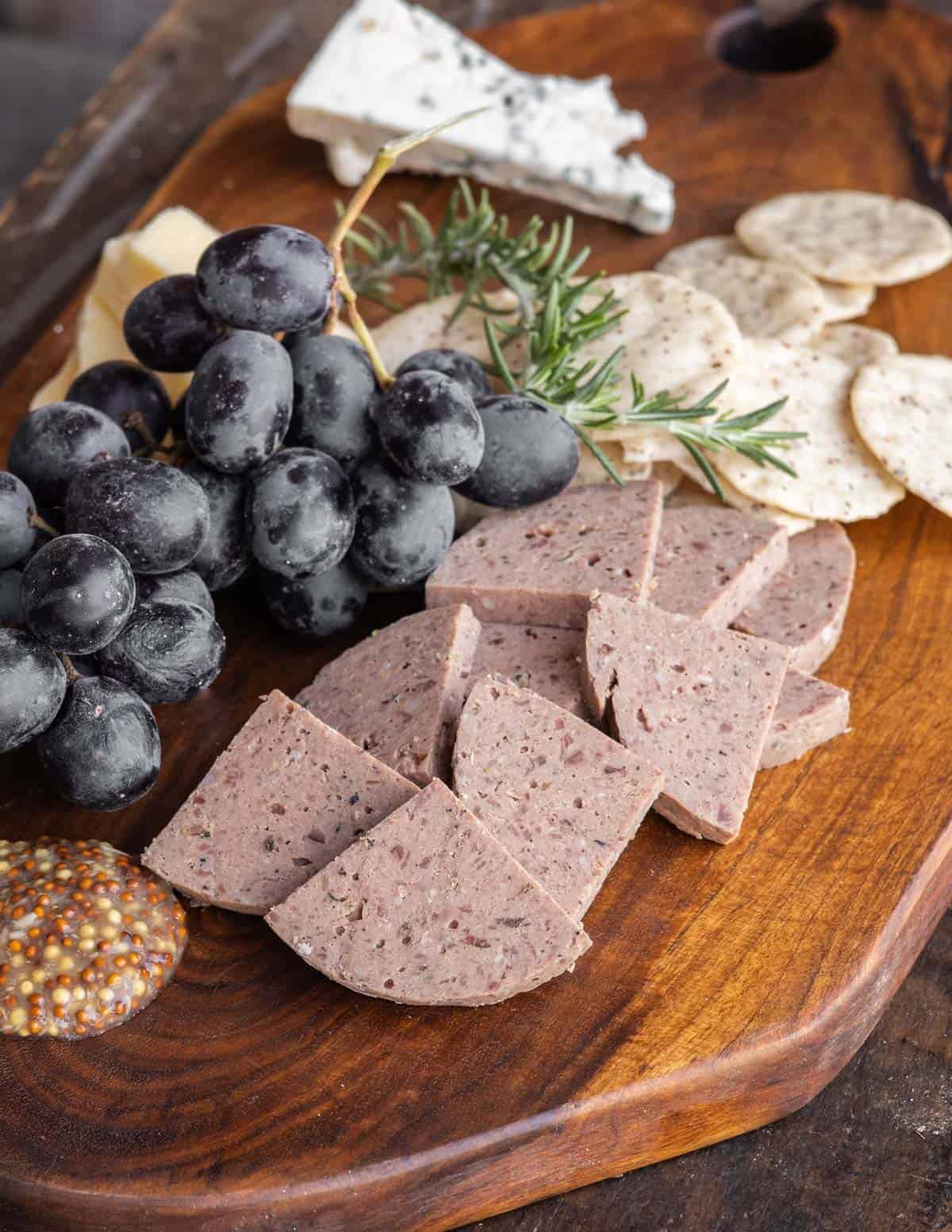 A charcuterie board filled with liverwurst, grapes, cheese and crackers. 