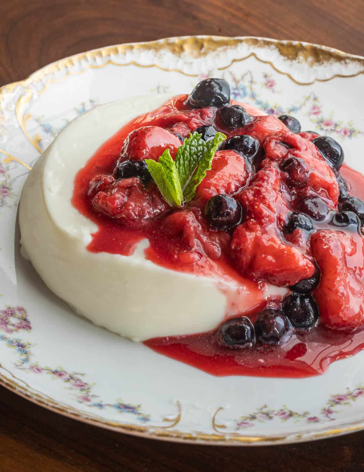A panna cotta topped with stewed strawberries and blueberries on a china plate.