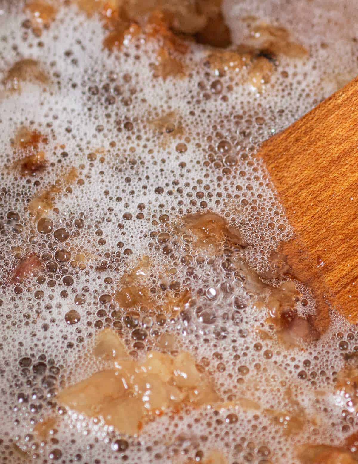 A spatula in a pot of cooking beef tallow showing bubbles rising to the surface. 