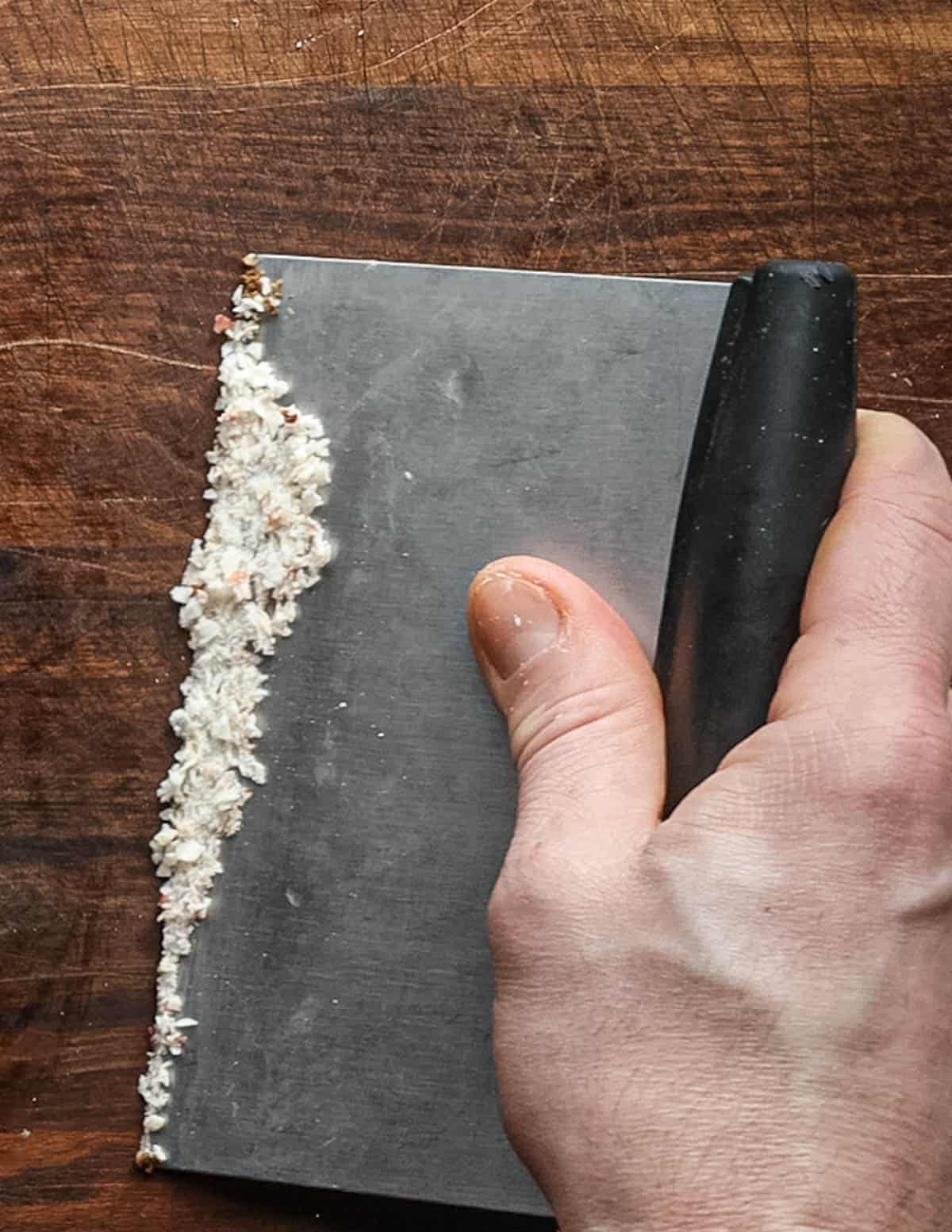 Cleaning beef fat from a cutting board using a bench scraper.
