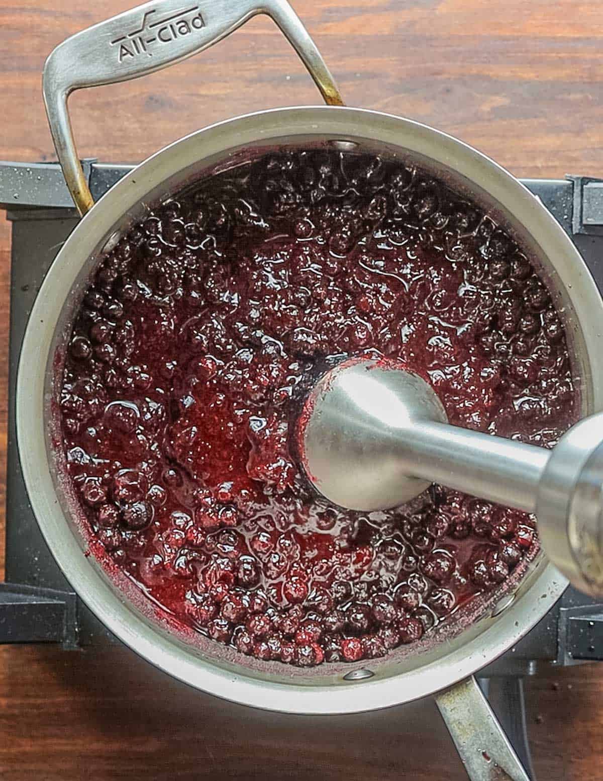 Pureeing a pot of cooking black currants with a hand blender. 