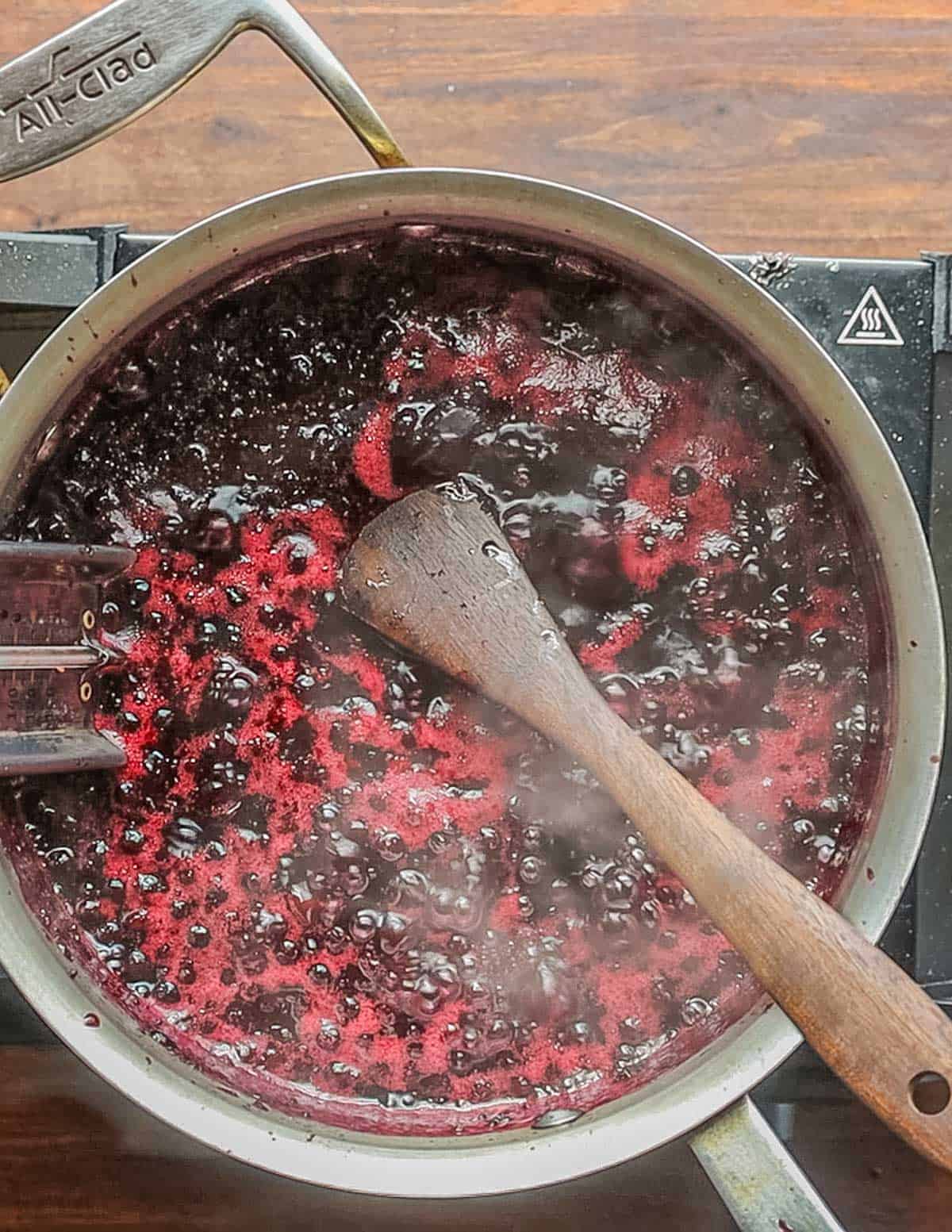 A pot of boiling black currant jam being stirred with a wooden spoon. 