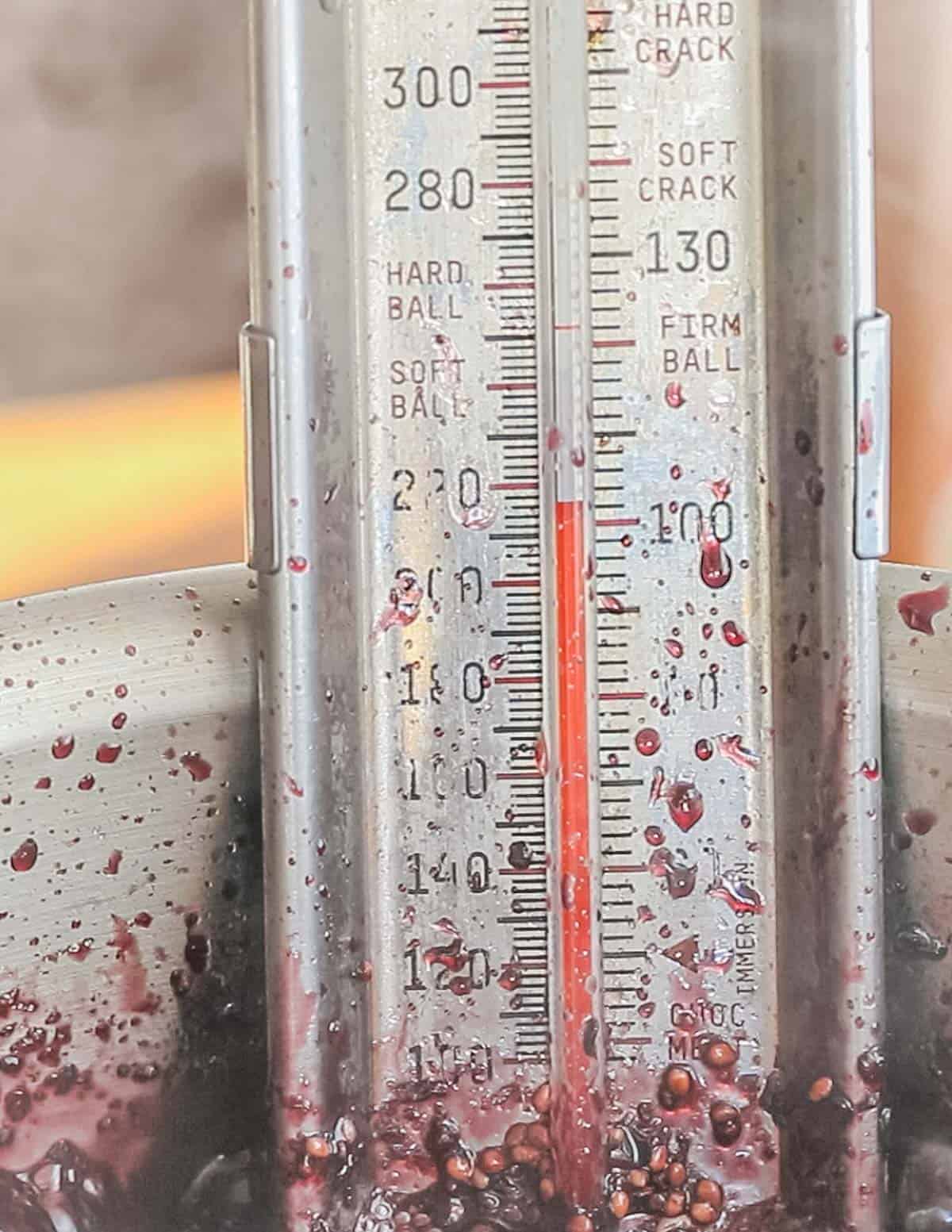 A close up image of a candy thermometer in a pot of jam showing 215 F. 