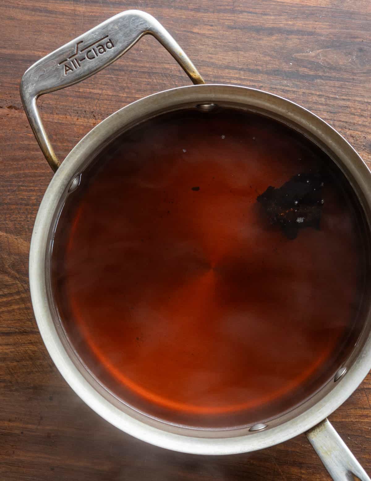 A piece of chaga mushroom cooking in a pot of water for 30 minutes, showing the change in color from tan to reddish brown. 