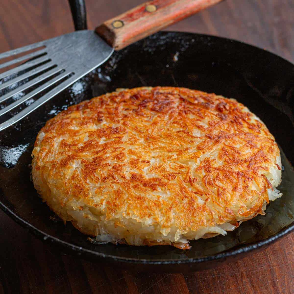 A perfectly cooked golden brown pan of homemade hashbrowns in a cast iron skillet. 