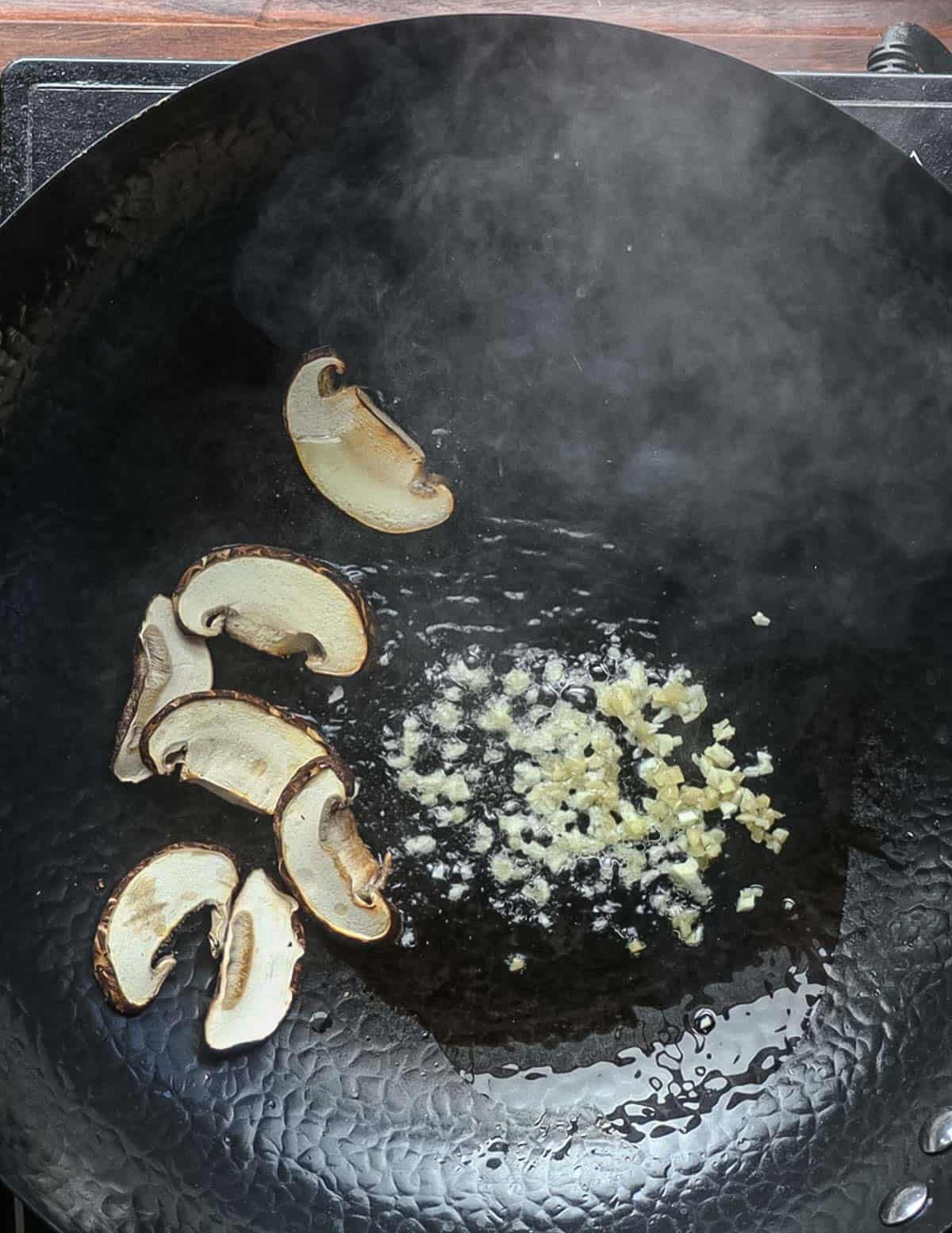 Adding chopped garlic and ginger to a wok with mushrooms. 