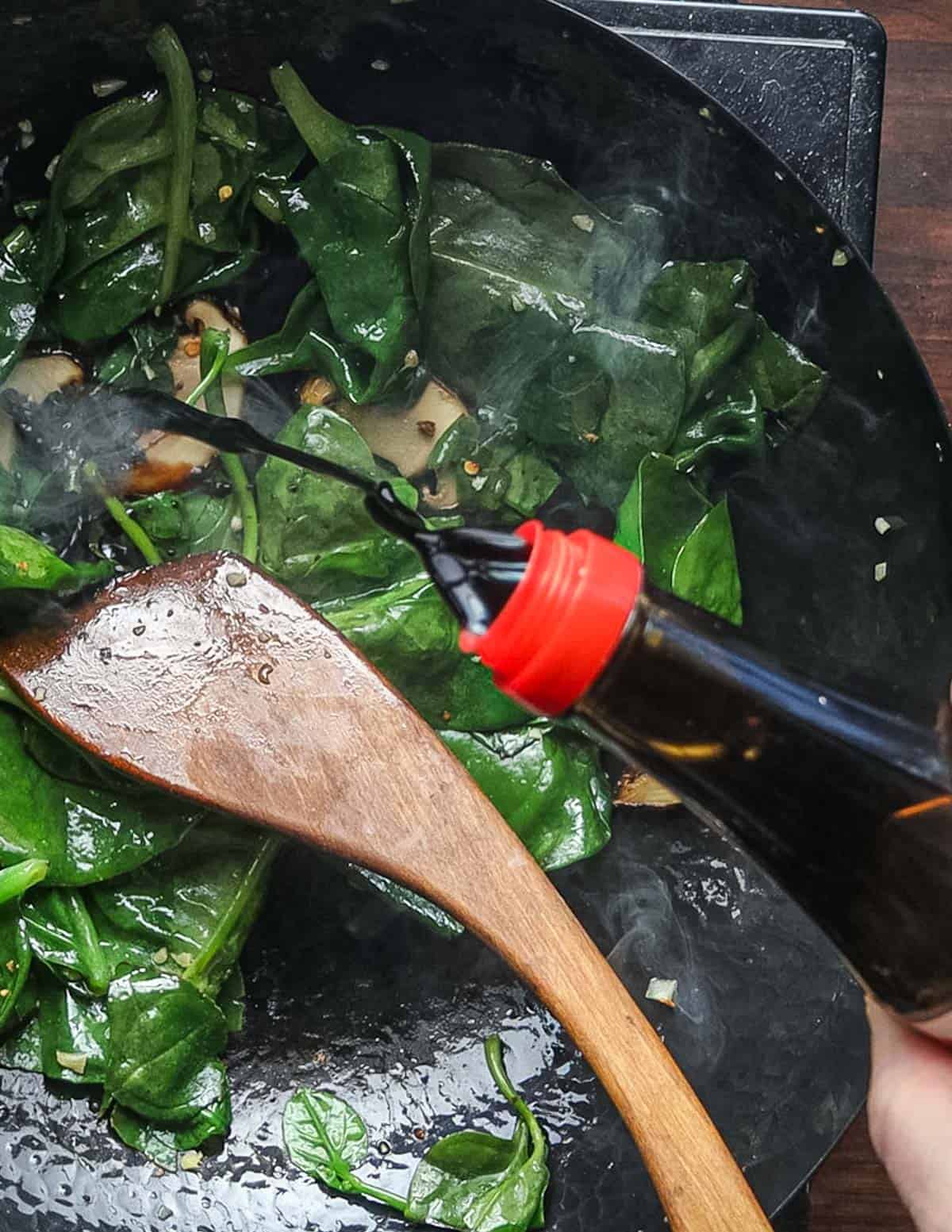 Adding soy sauce to a wok with malabar spinach leaves and mushrooms. 