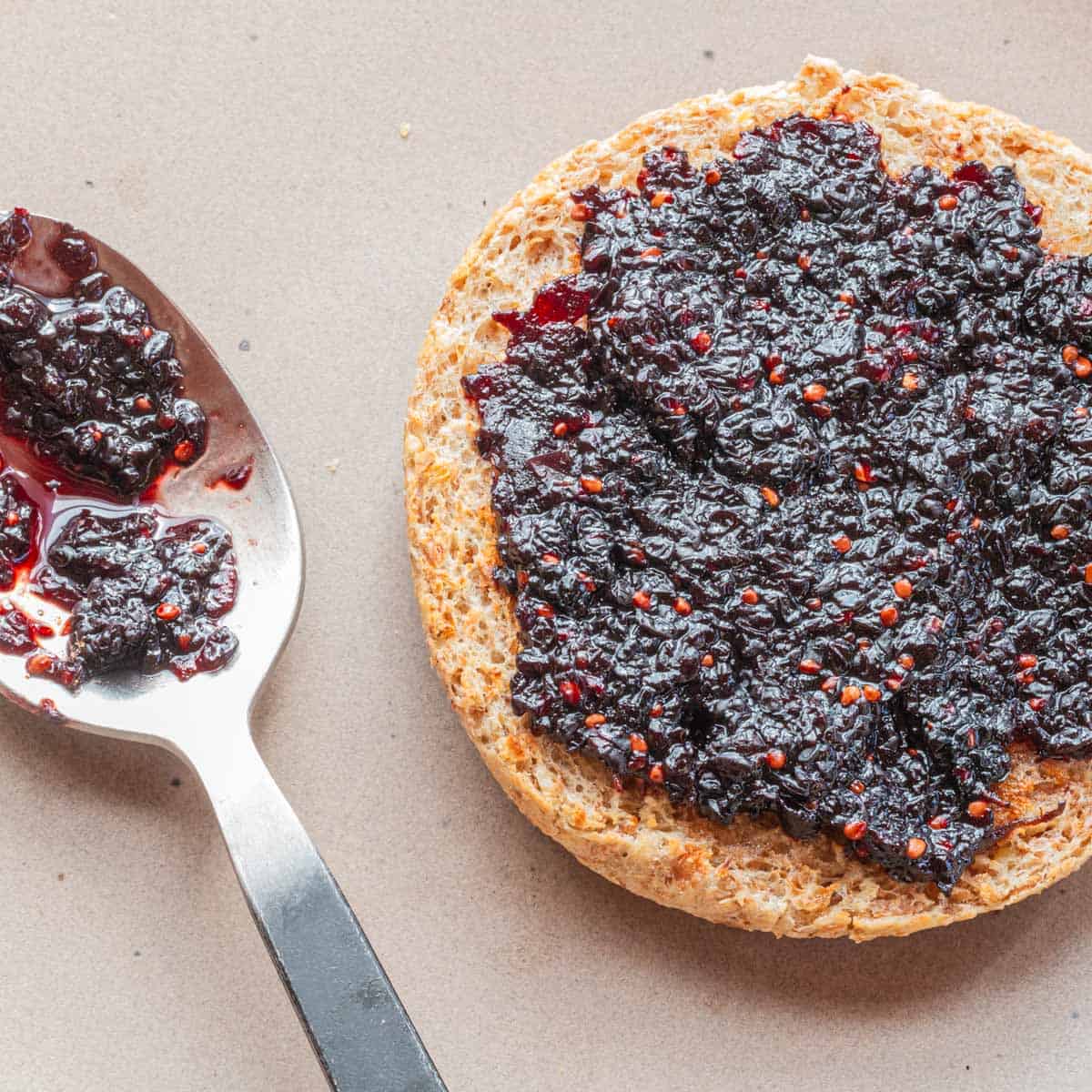 A buttered English muffin spread with mulberry jam. 