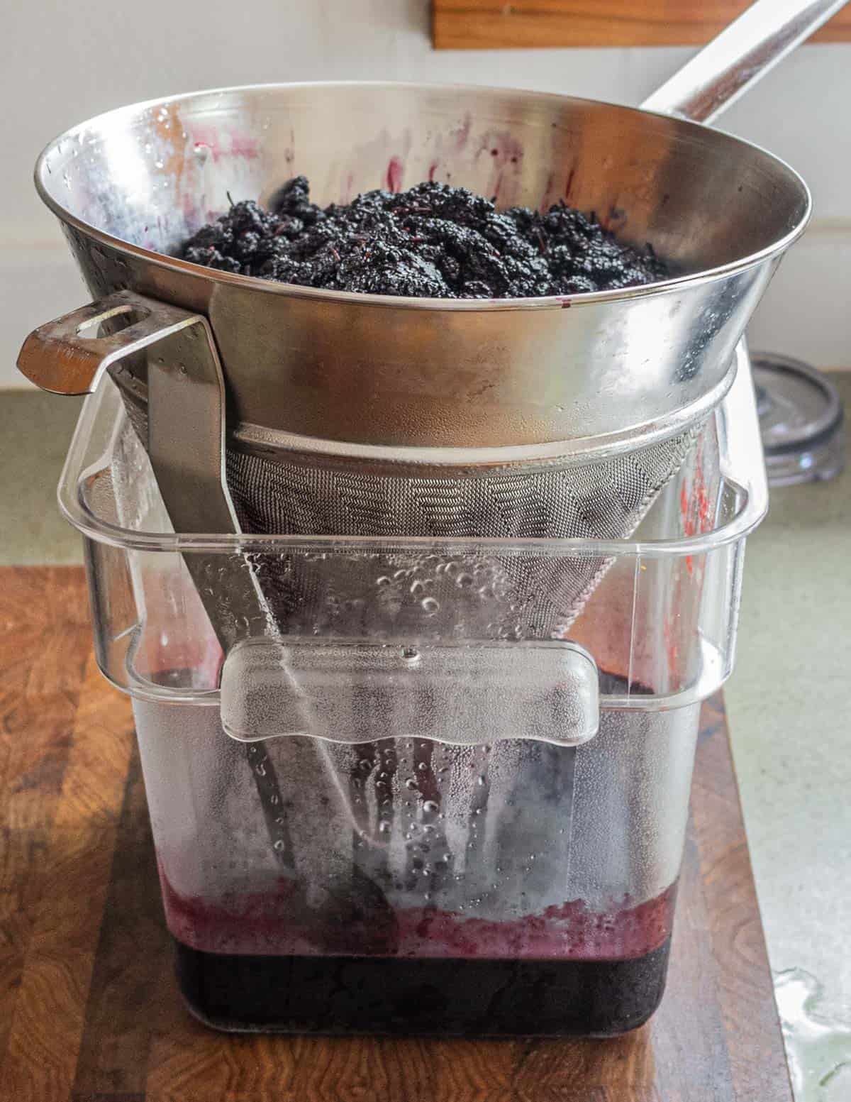Straining mulberry juice over a container using a mesh strainer. 
