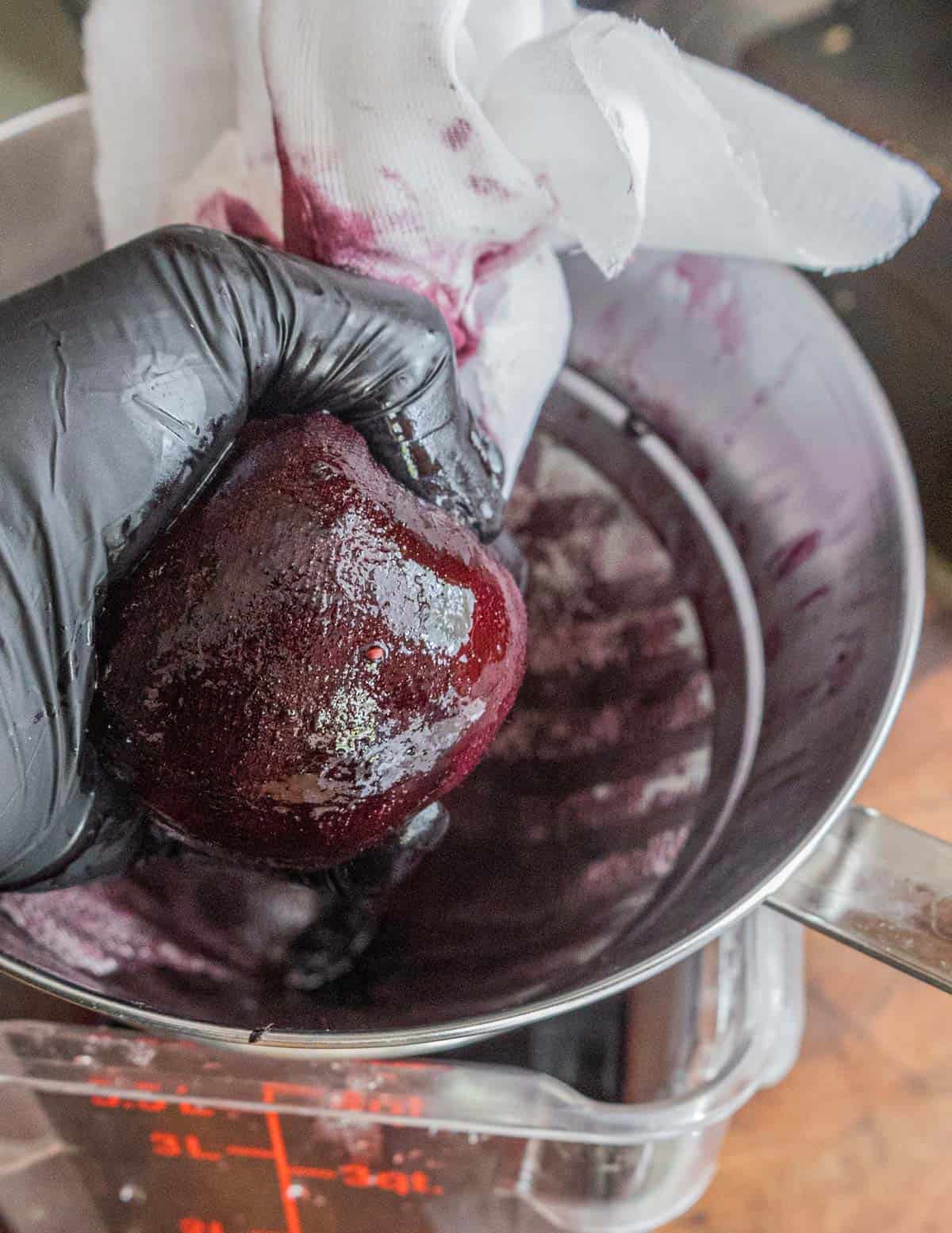 A gloved hand squeezing juice from cooked mulberries wrapped in cheesecloth. 