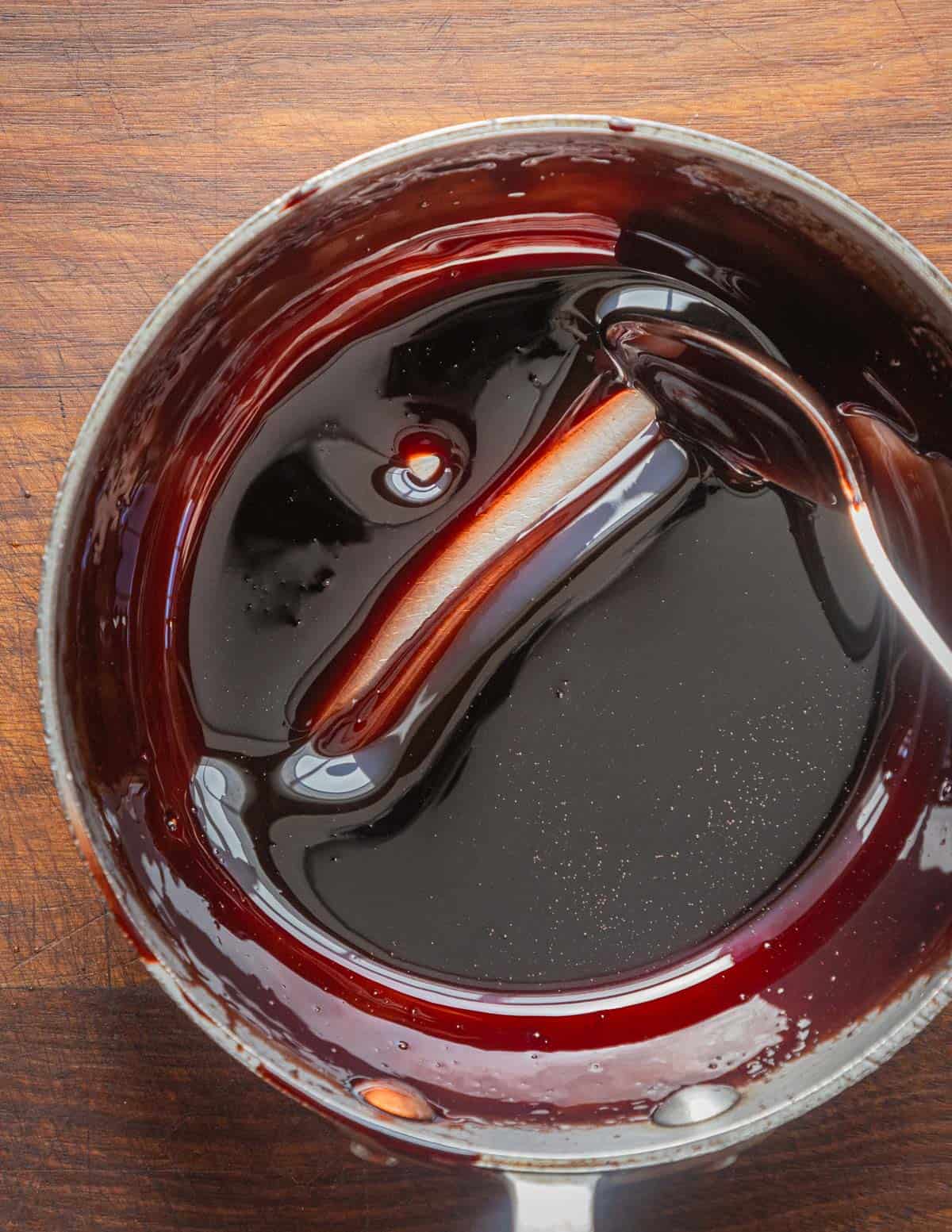 A spoon being dragged through a finished pot of mulberry syrup showing the bottom of the pan. 