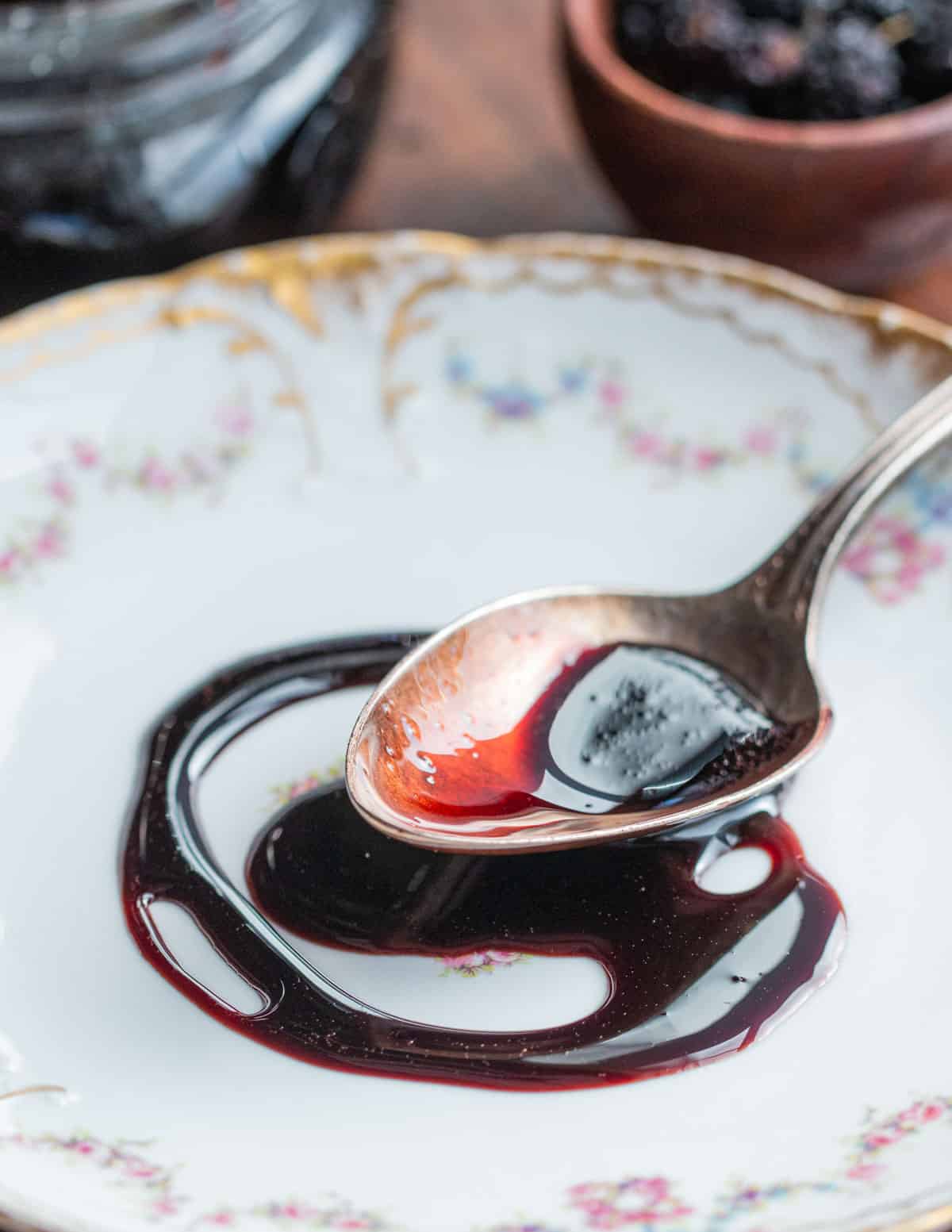 A spoonful of black mulberry syrup also known as pekmez or petimezi molasses on a china plate next to a bowl of fresh mulberries. 