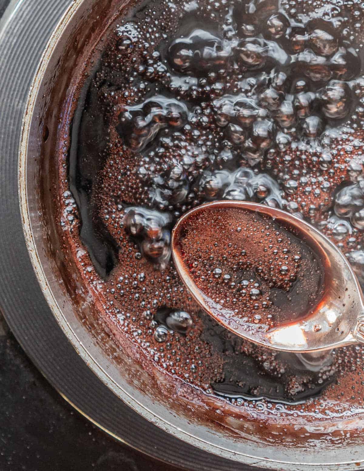 A spoon in a pot of mulberry syrup removing impurities. 