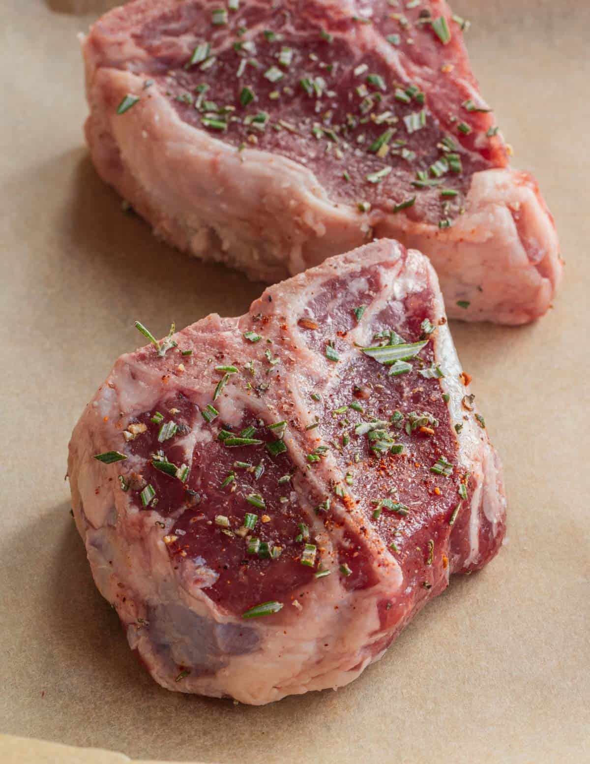Lamb loin chops seasoned with rosemary on a baking sheet lined with parchment.