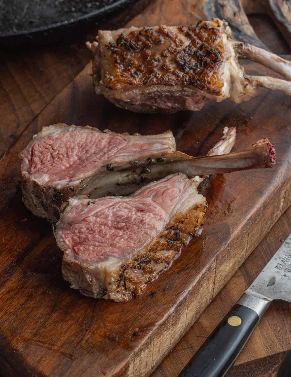 A carved rack of lamb showing two rib chops on a cutting board ready to eat.