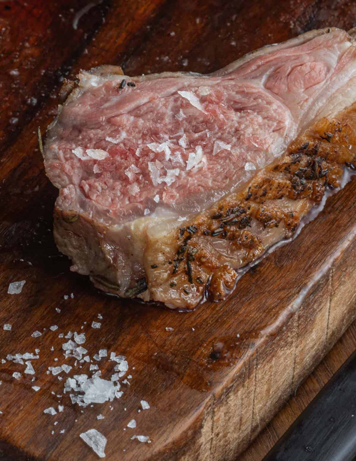 A sliced pink lamb rib chop cooked sous vide garnished with flaky salt. 