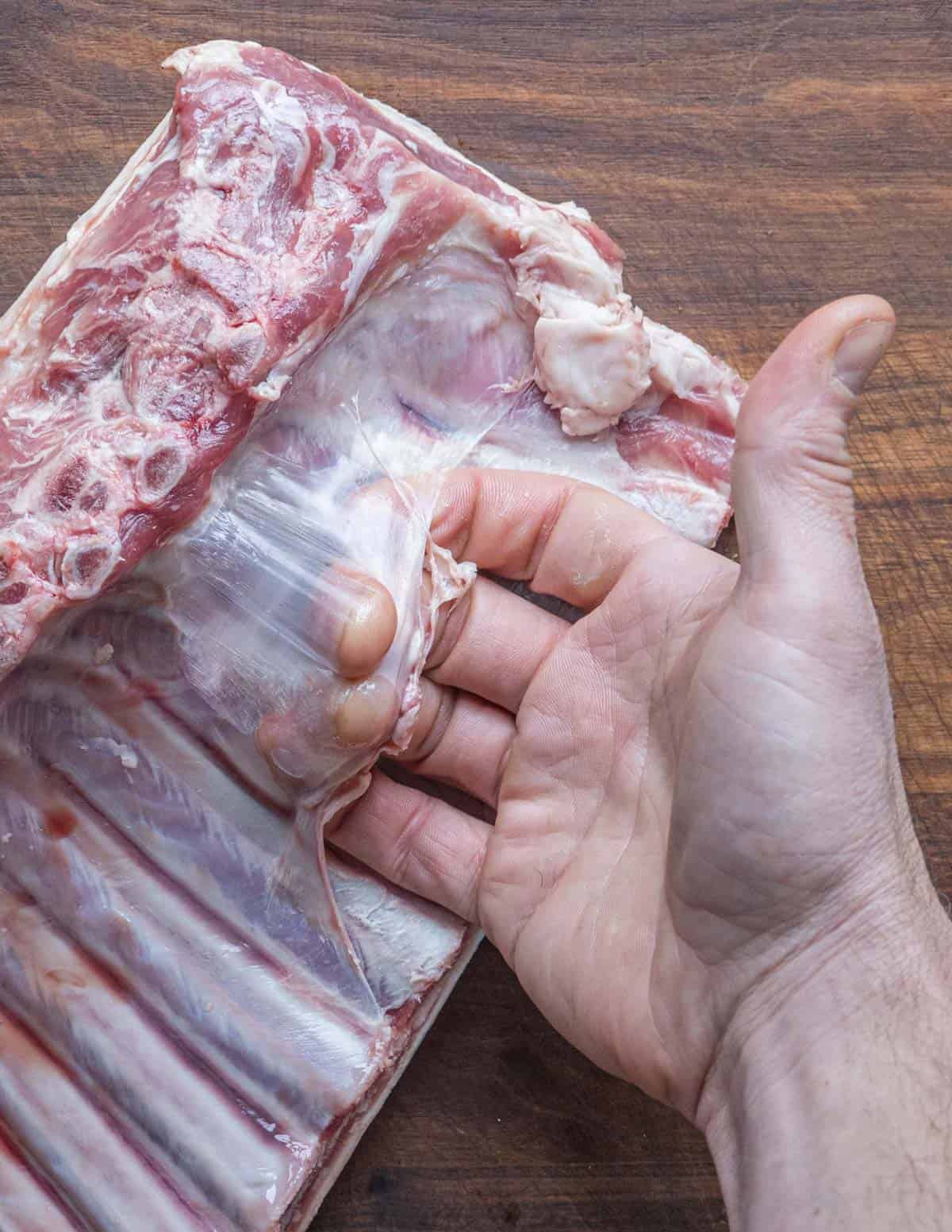 Removing the membrane from underneath a rack of lamb by hand. 