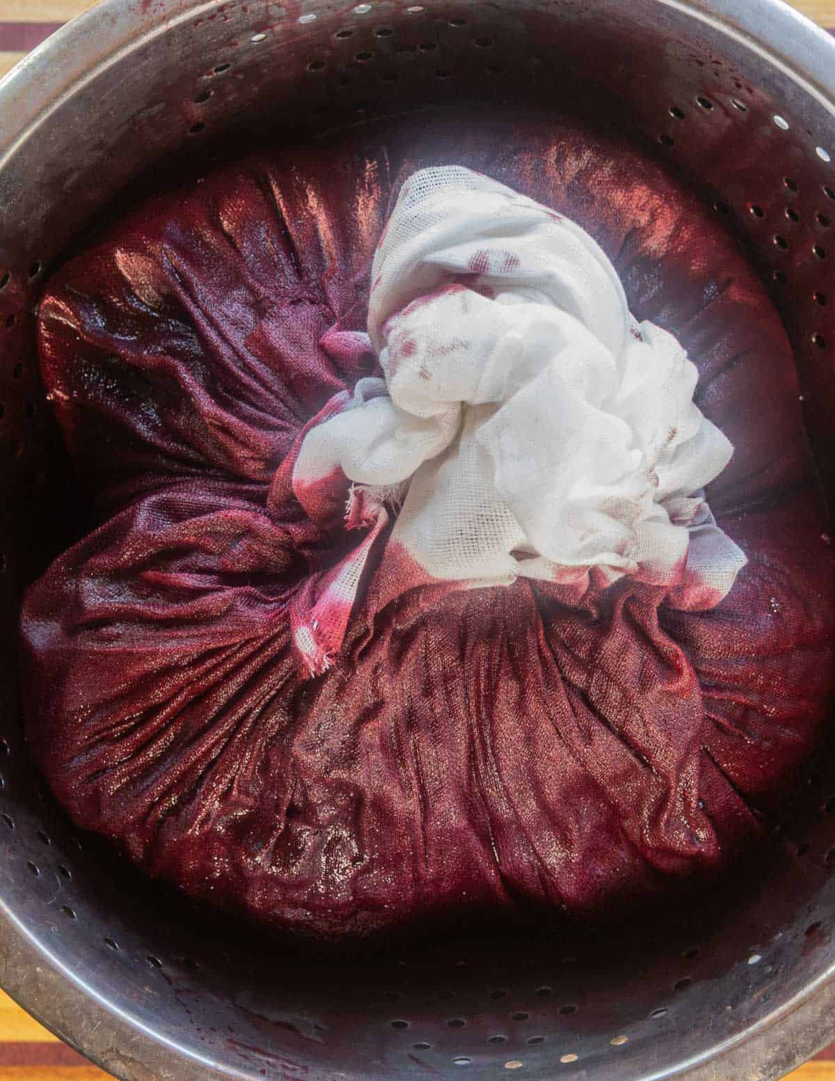 A bag of cheesecloth filled with grapes being juiced. 