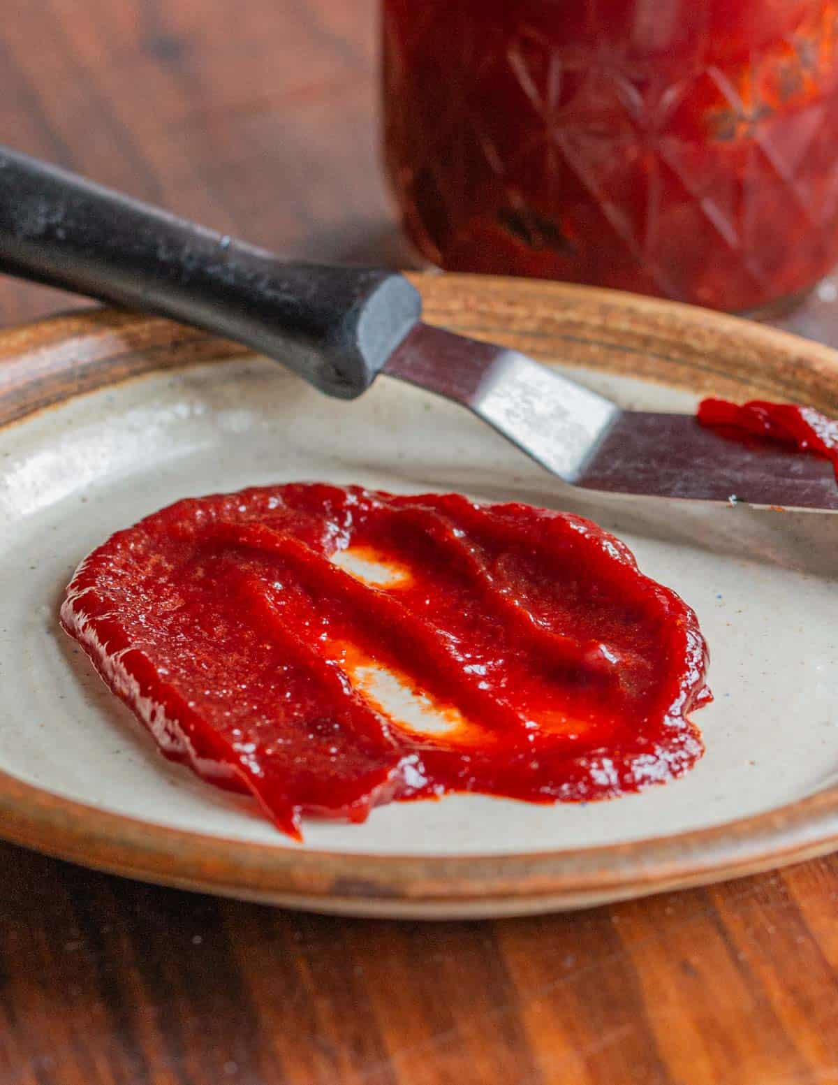 A spoonful of wild plum butter spread on a plate next to a spatula. 