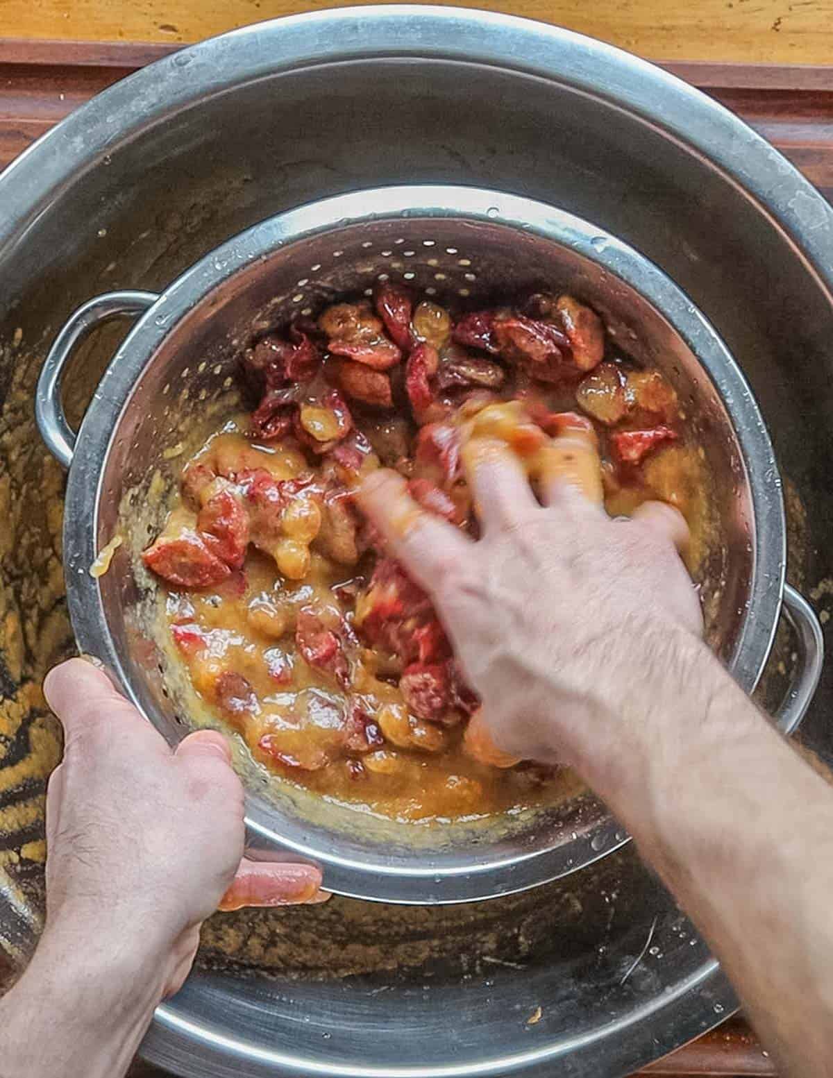 Mashing crushed plums in a colander to extract the plum puree. 