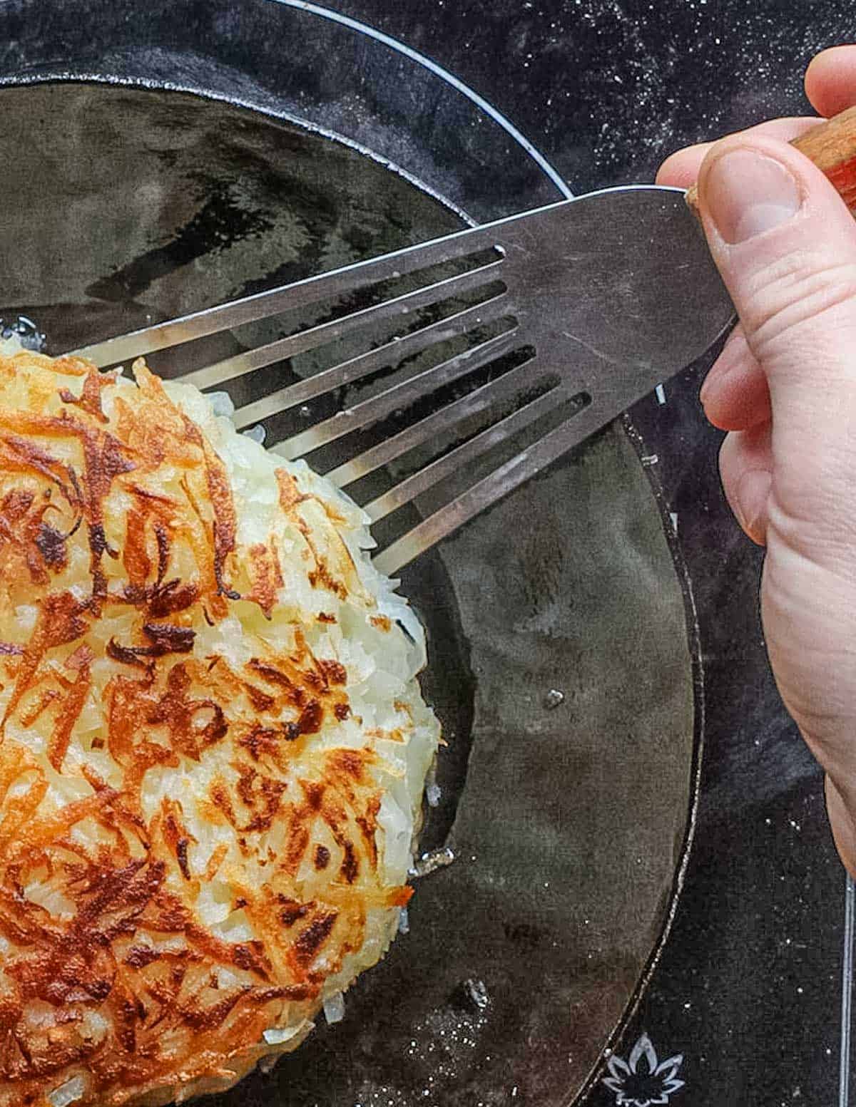 Flipping hashbrowns in a cast iron pan with a spatula. 