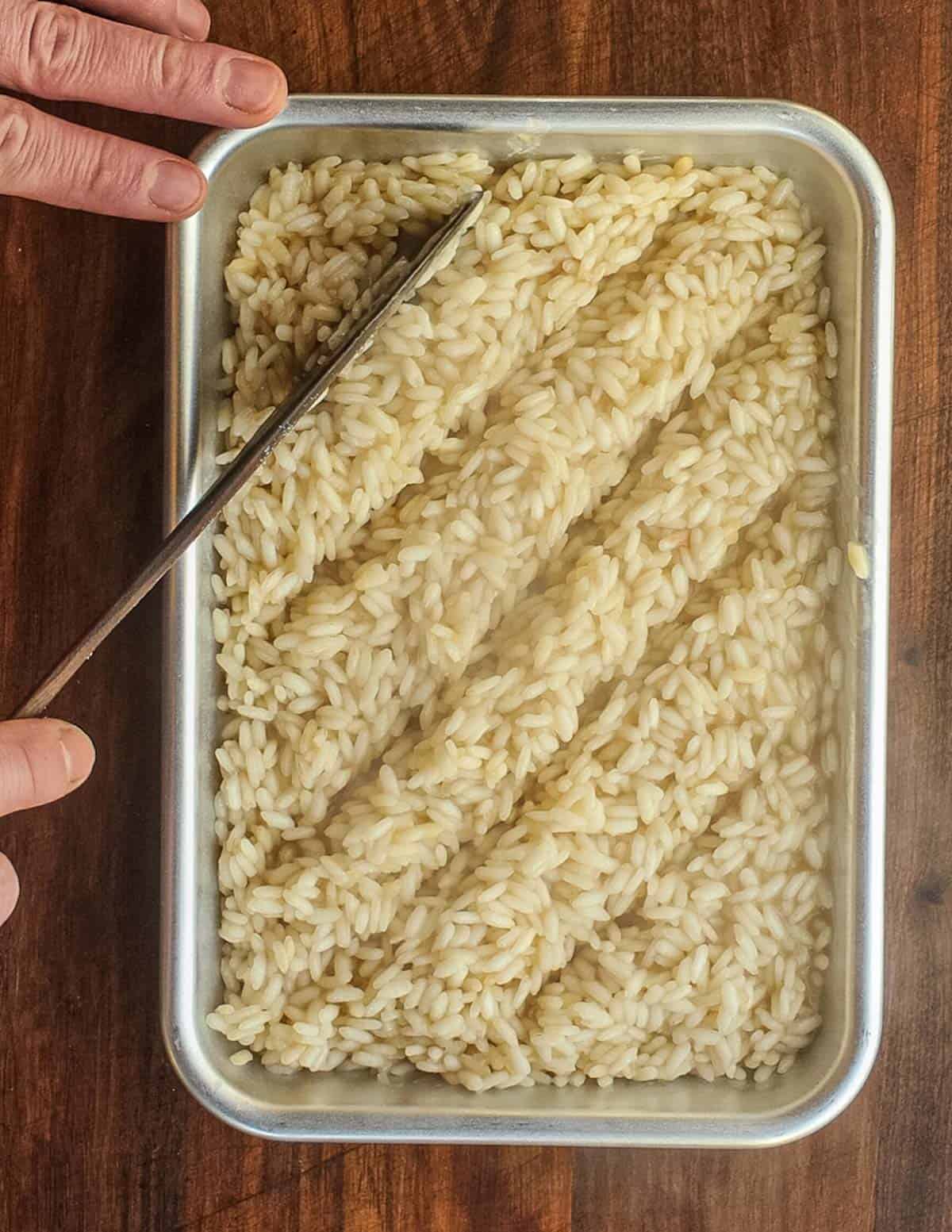 Spreading pre-cooked risotto rice on a tray with a spatula. 