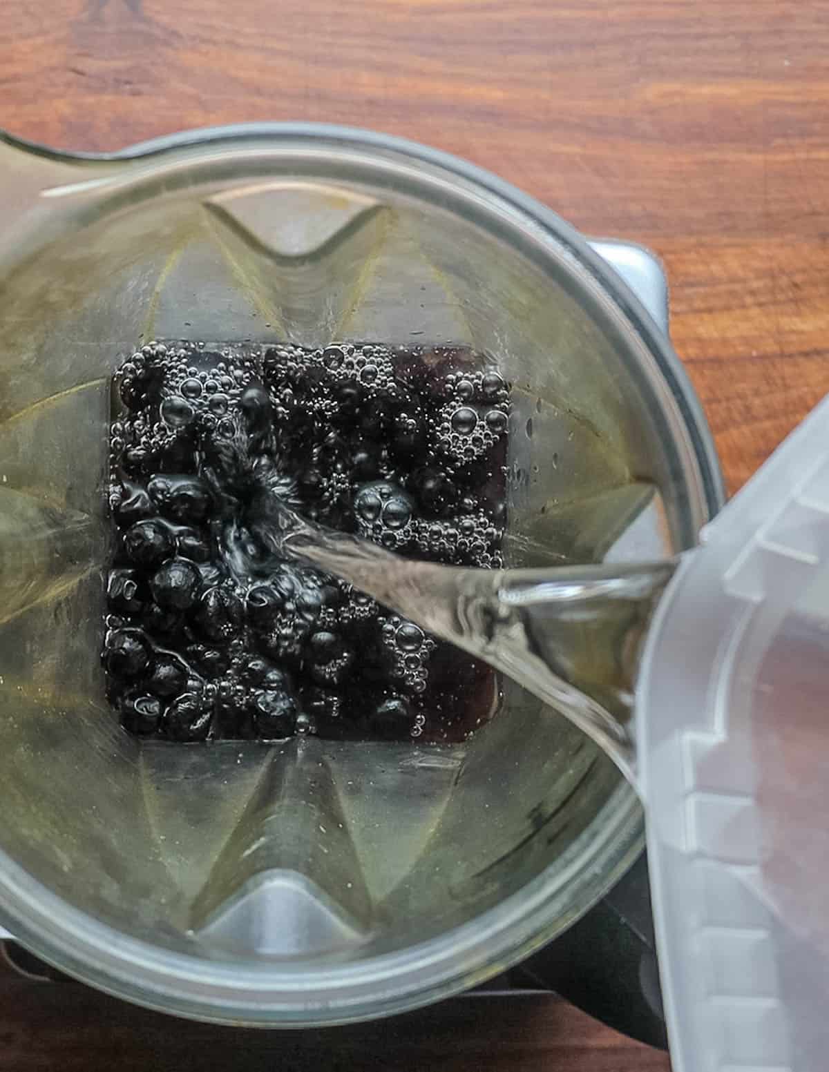 Adding water to black chokeberries in a blender. 