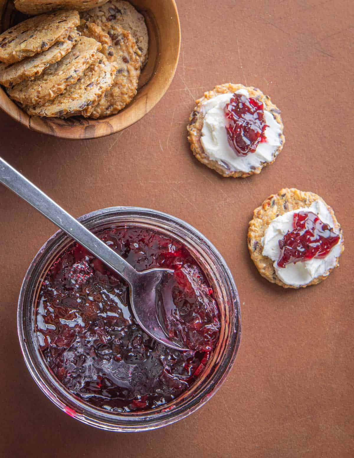 Aronia hot pepper jelly on crackers with goat cheese next to a jar of jelly and a bowl of crackers. 