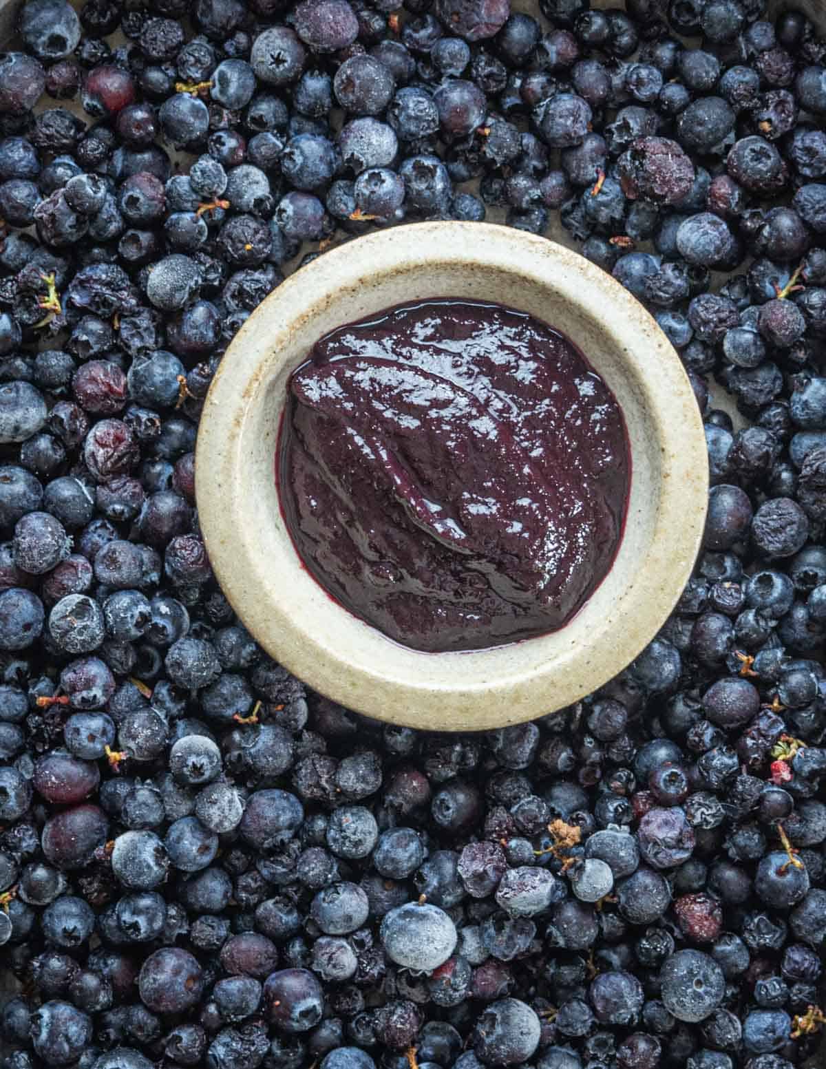 Blueberry barbecue sauce made from fresh wild blueberries in a cup surrounded by wild blueberries. 