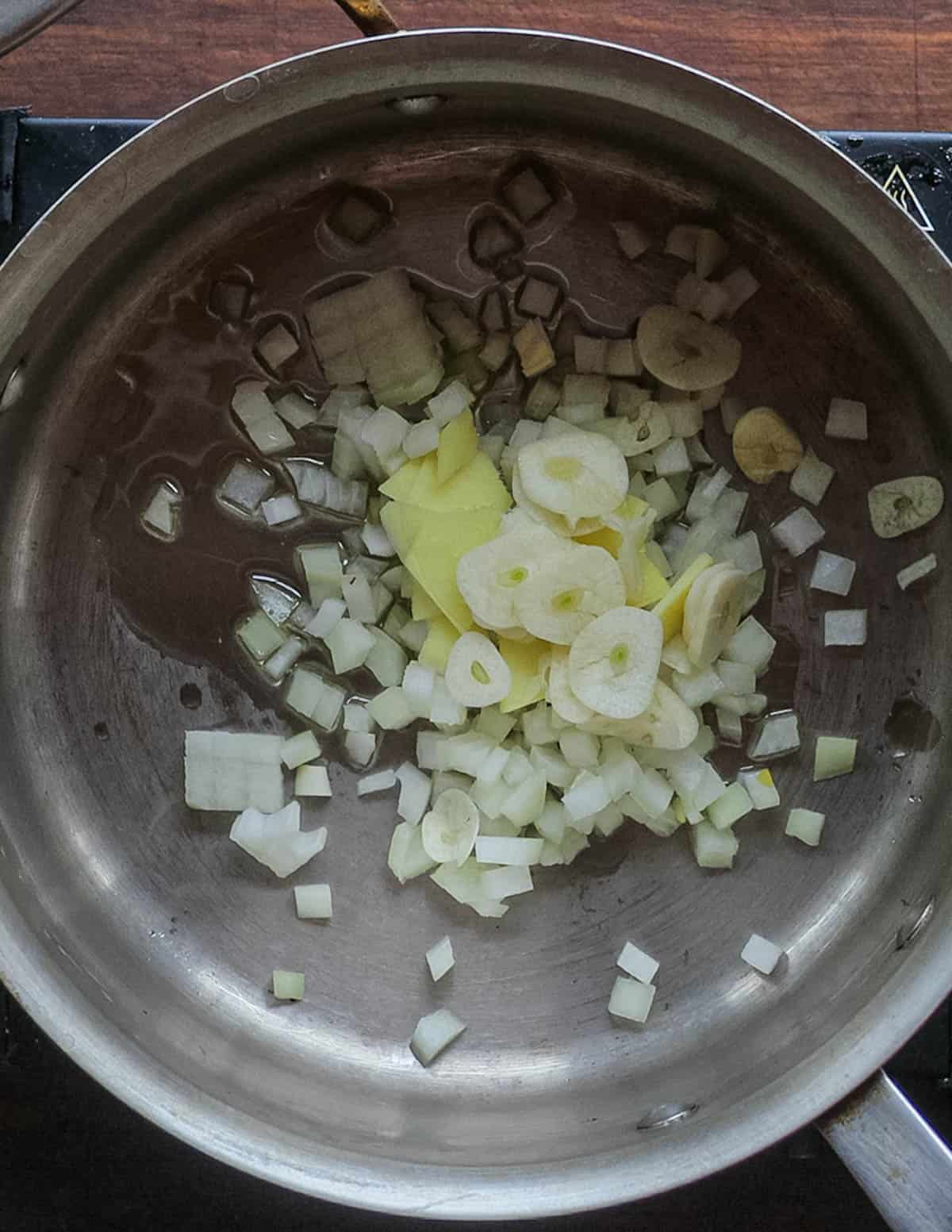 Adding onion, garlic, ginger and shallot to a pan and cooking in oil.