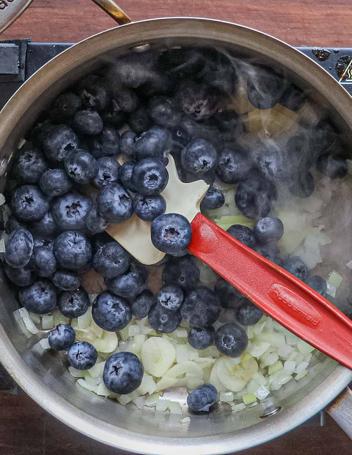 Adding fresh blueberries to a pan of shallot, ginger and garlic.