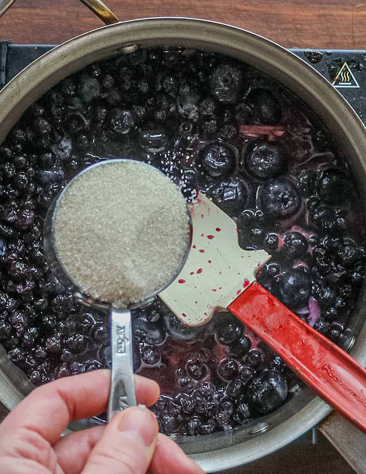 Adding a cup of sugar to a pan of cooking blueberry sauce.