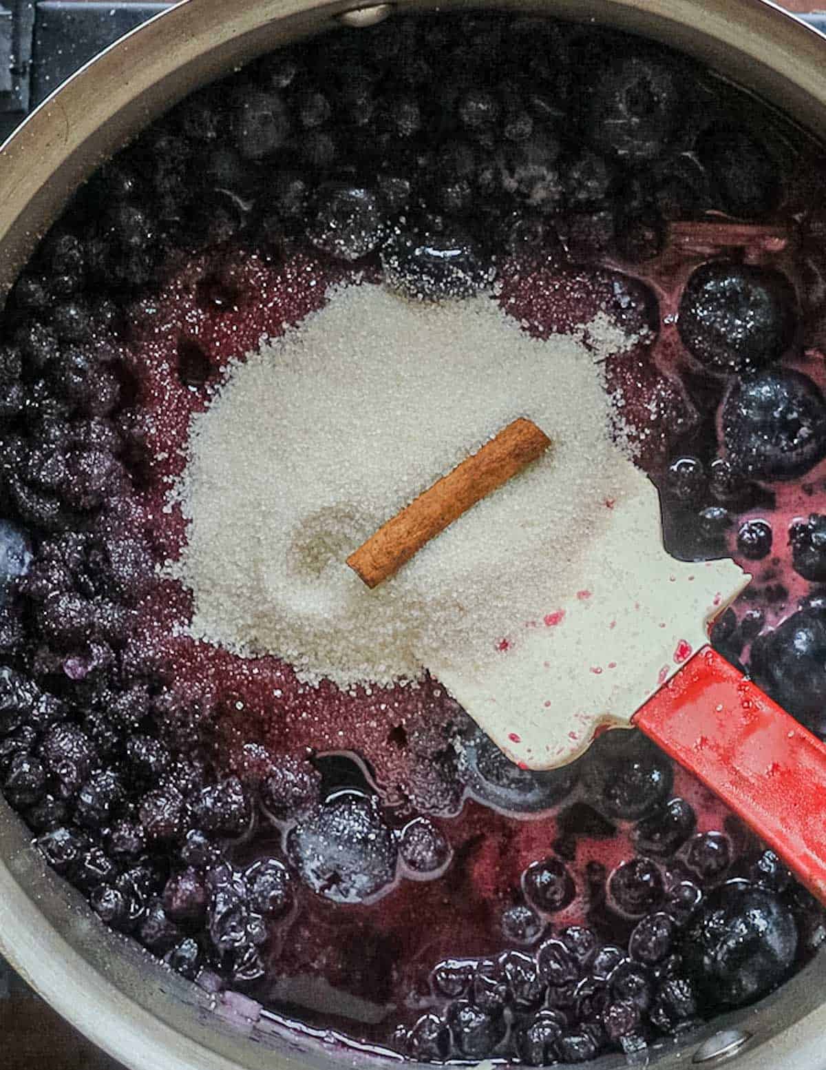 Adding a cinnamon stick to a pan of blueberries cooking.