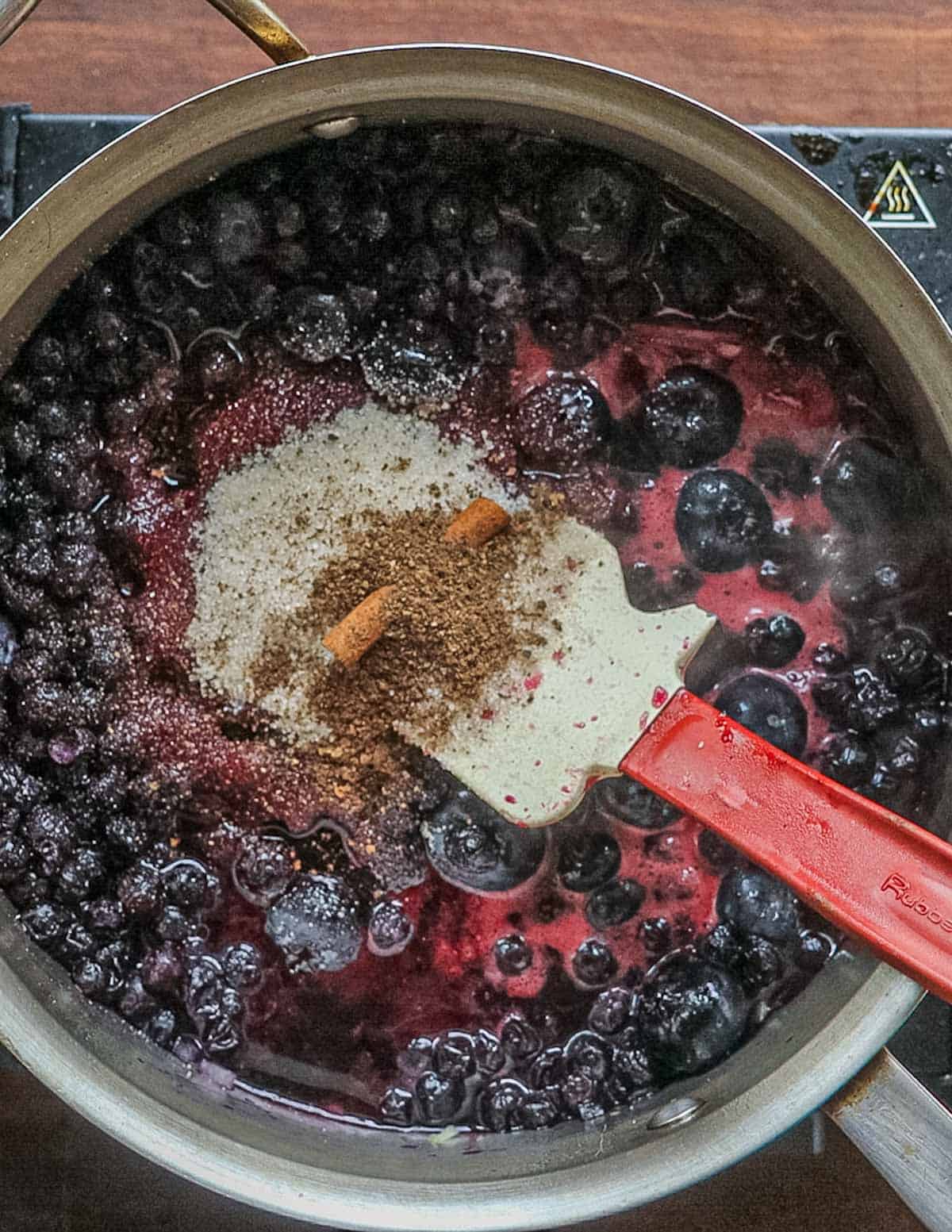 Adding ground allspice to a pan of cooking blueberry sauce.