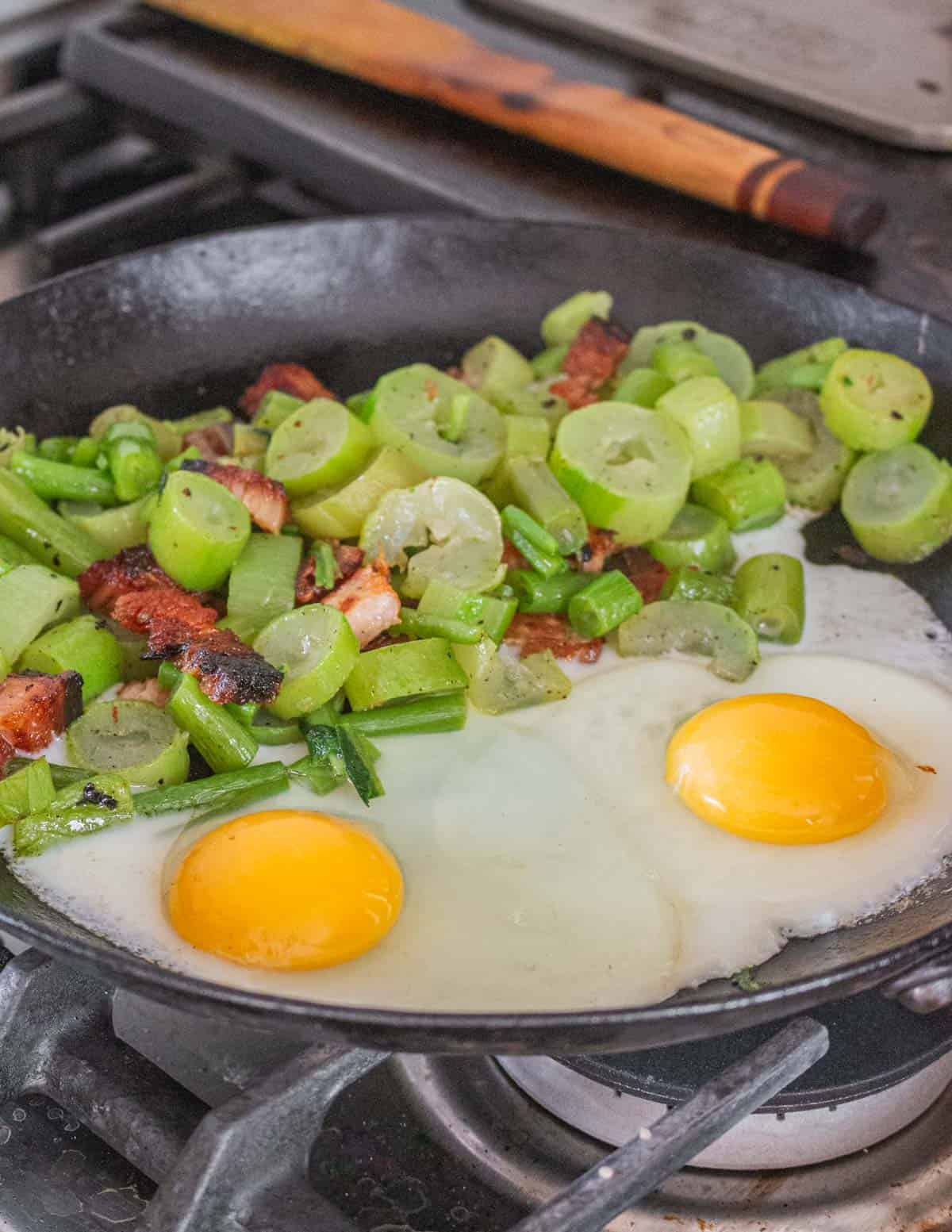 Adding eggs to a pan of cooking poke sallet greens and bacon. 
