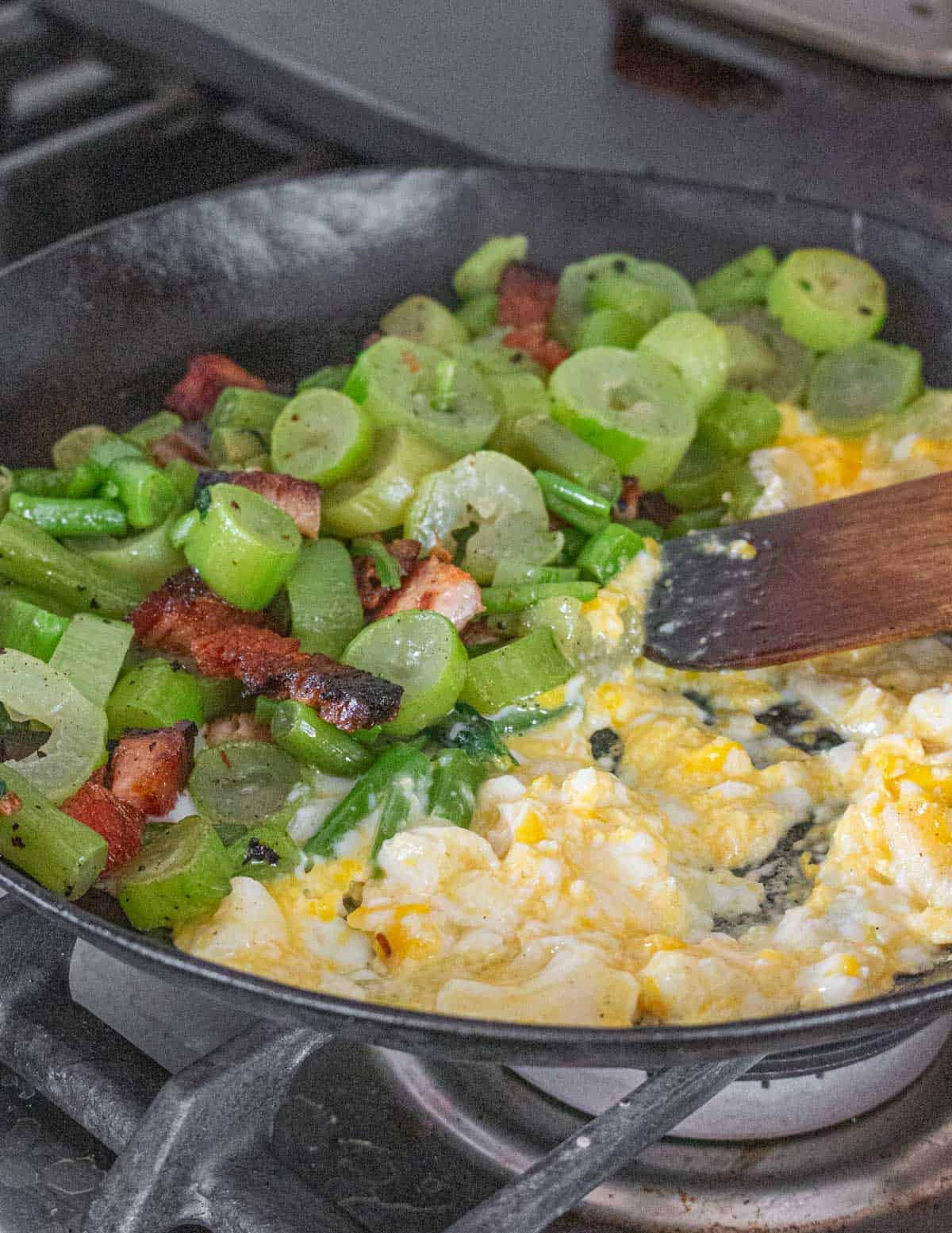 Stirring scrambled eggs with a spatula in a cast iron pan. 