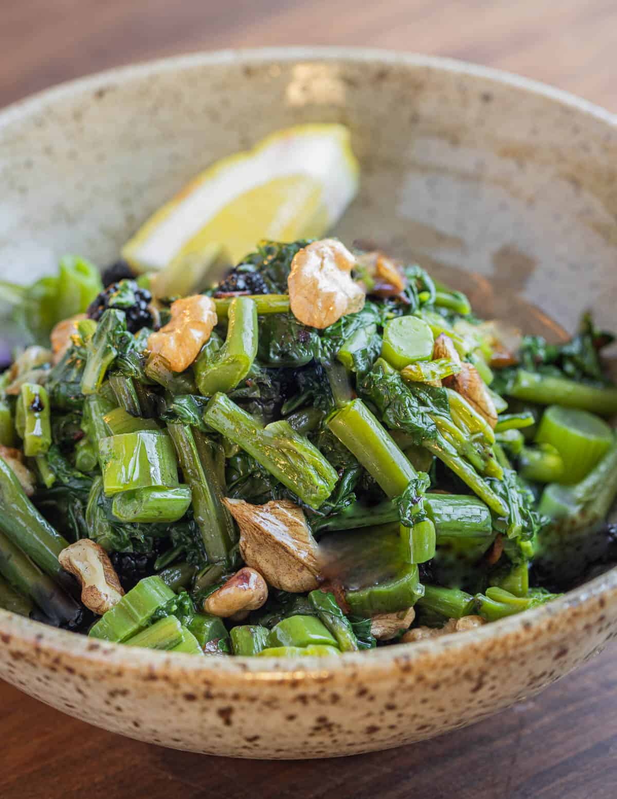 A bowl of cooked pokweed greens with butternuts olive oil and lemon. 