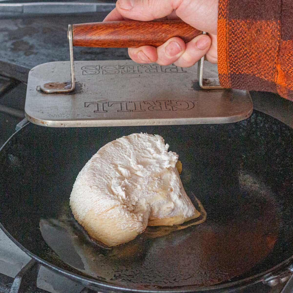 A lions mane mushroom cooking in a pan after it's been dipped in flour. 
