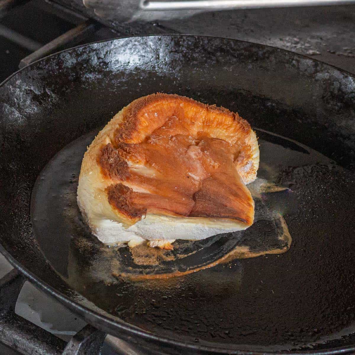A golden brown lions mane mushroom steak cooking in a pan. 