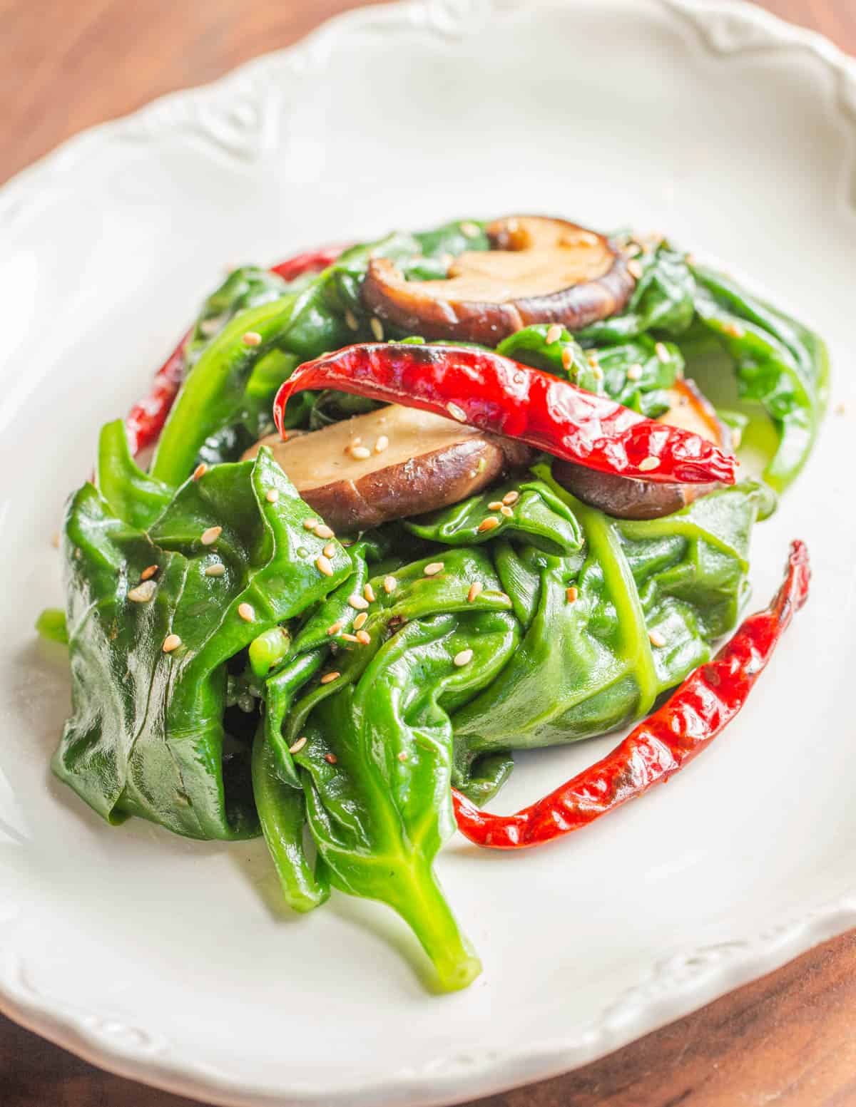 A dish of stir fried malabar spinach garnished with sesame oil and sesame seeds. 