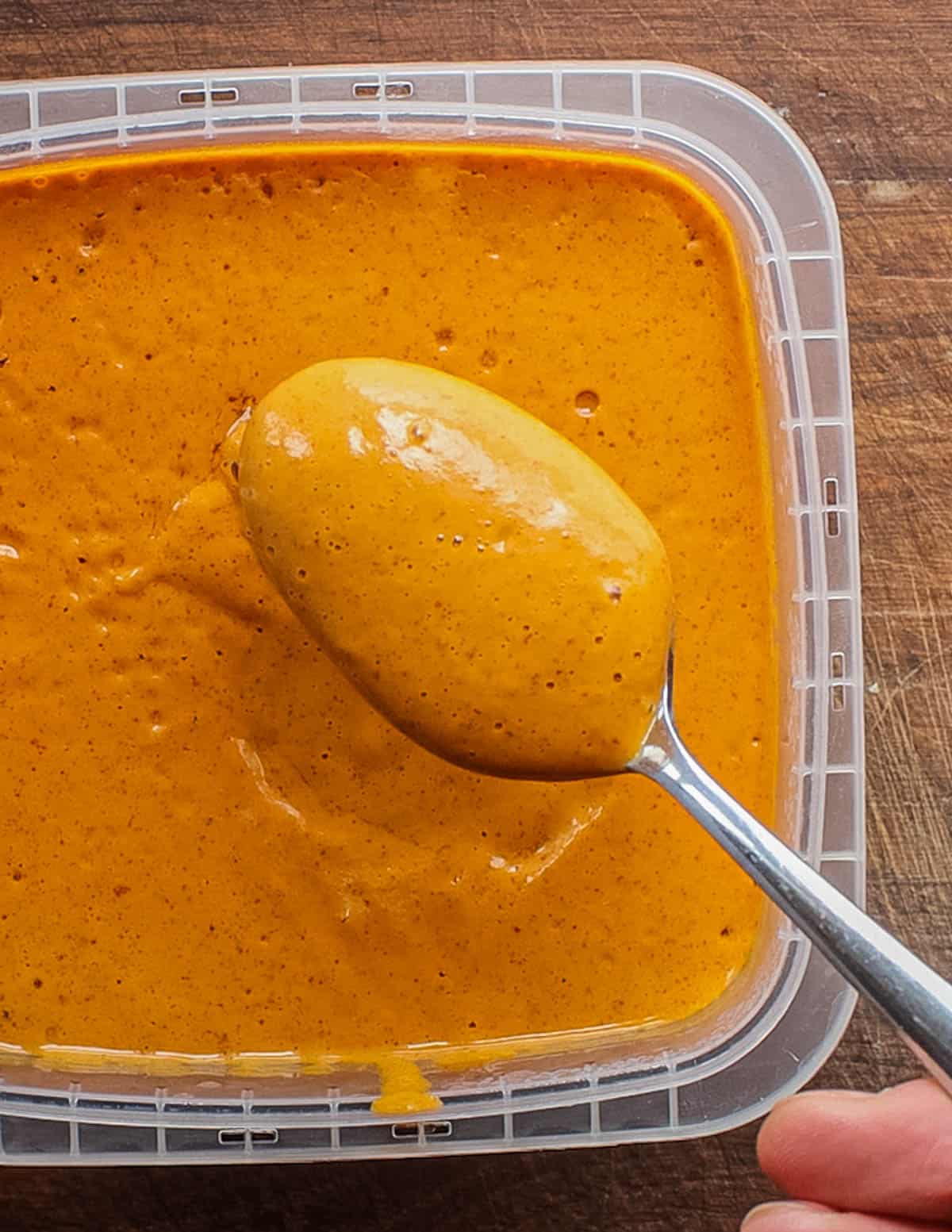 A spoon serving an orange honey mustard barbecue sauce. 