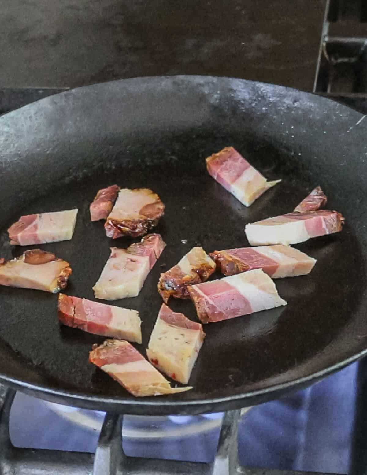 Slices of bacon in a carbon steel pan cooking. 
