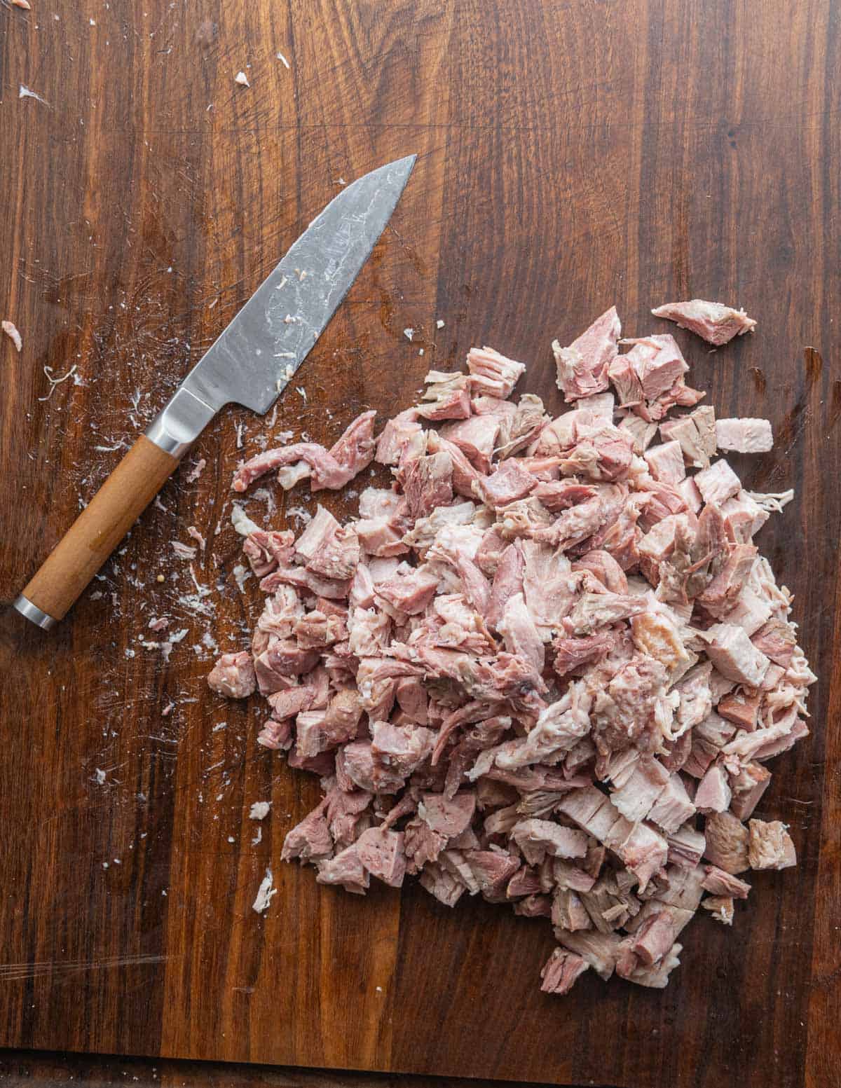 A utility knife next to diced pieces of pork jowl and pig head meat. 