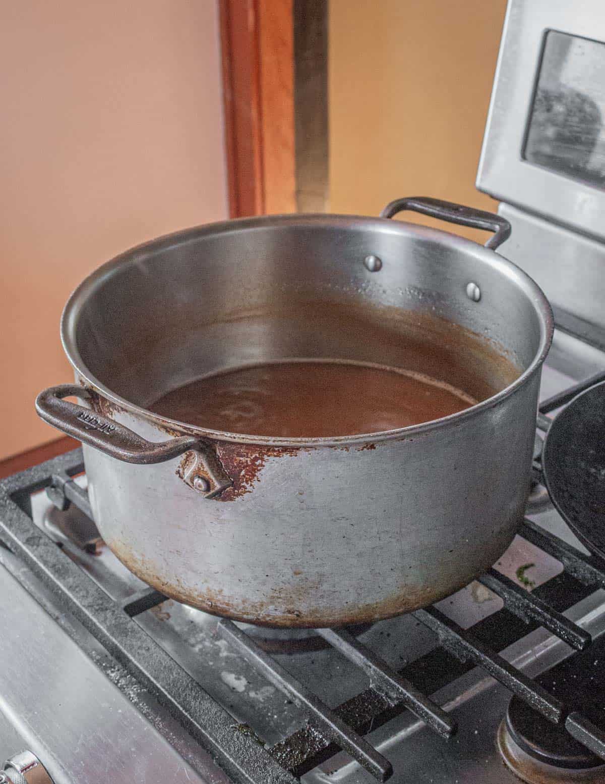 A pot of liquid from cooking pig heads reducing on the stove to ⅛th it's volume. 