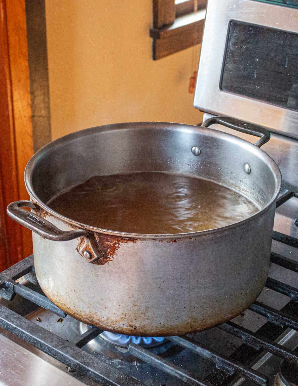 A pot full of liquid from cooking a pigs head reducing on the stove. 